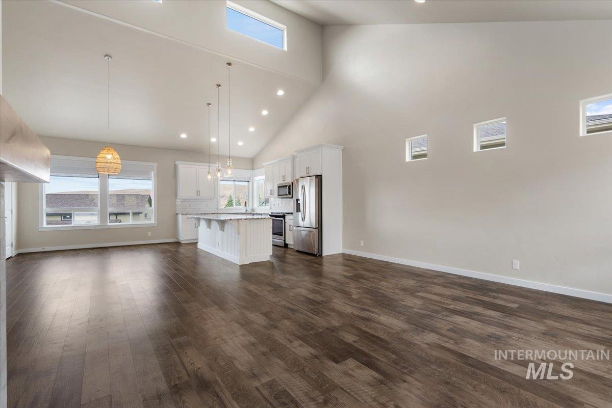 Unfurnished living room with high vaulted ceiling, recessed lighting, and dark wood-style floors