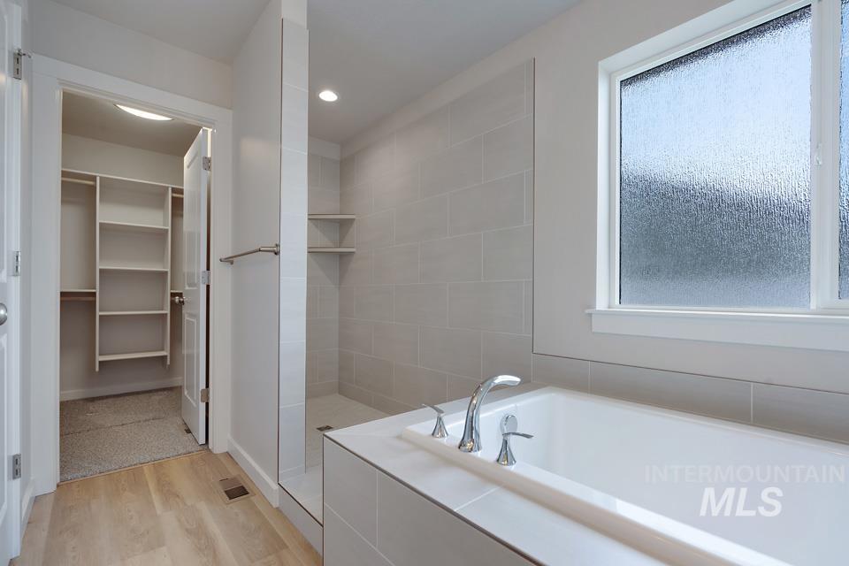 Full bathroom with a walk in closet, a bath, wood finished floors, a tile shower, and recessed lighting