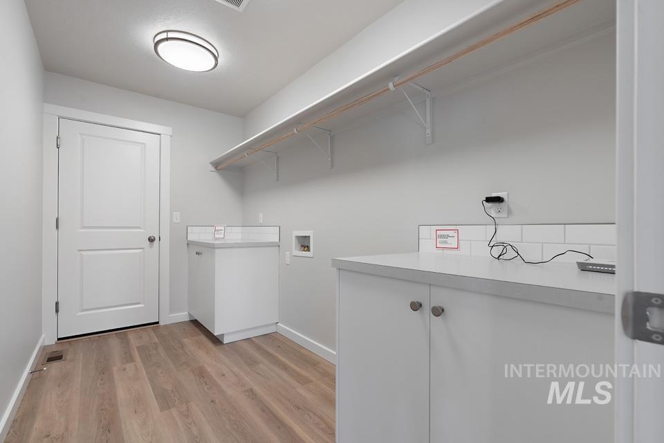 Laundry area with hookup for a washing machine, light wood-type flooring, and cabinet space