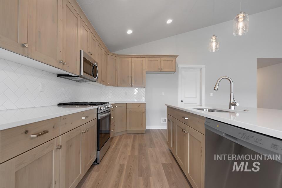 Kitchen with stainless steel appliances, light wood-type flooring, light countertops, light brown cabinets, and decorative backsplash