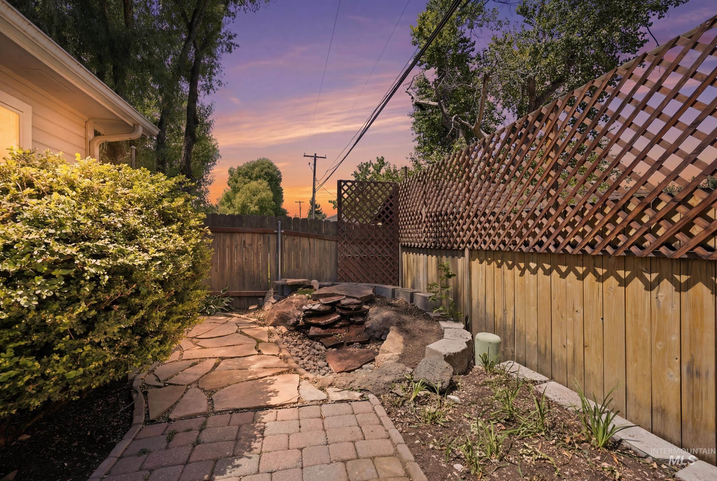 Backyard area featuring a flagstone pathway, a brick paver section, a natural stone water feature, a wood privacy fence, and an integrated wood lattice fence extension