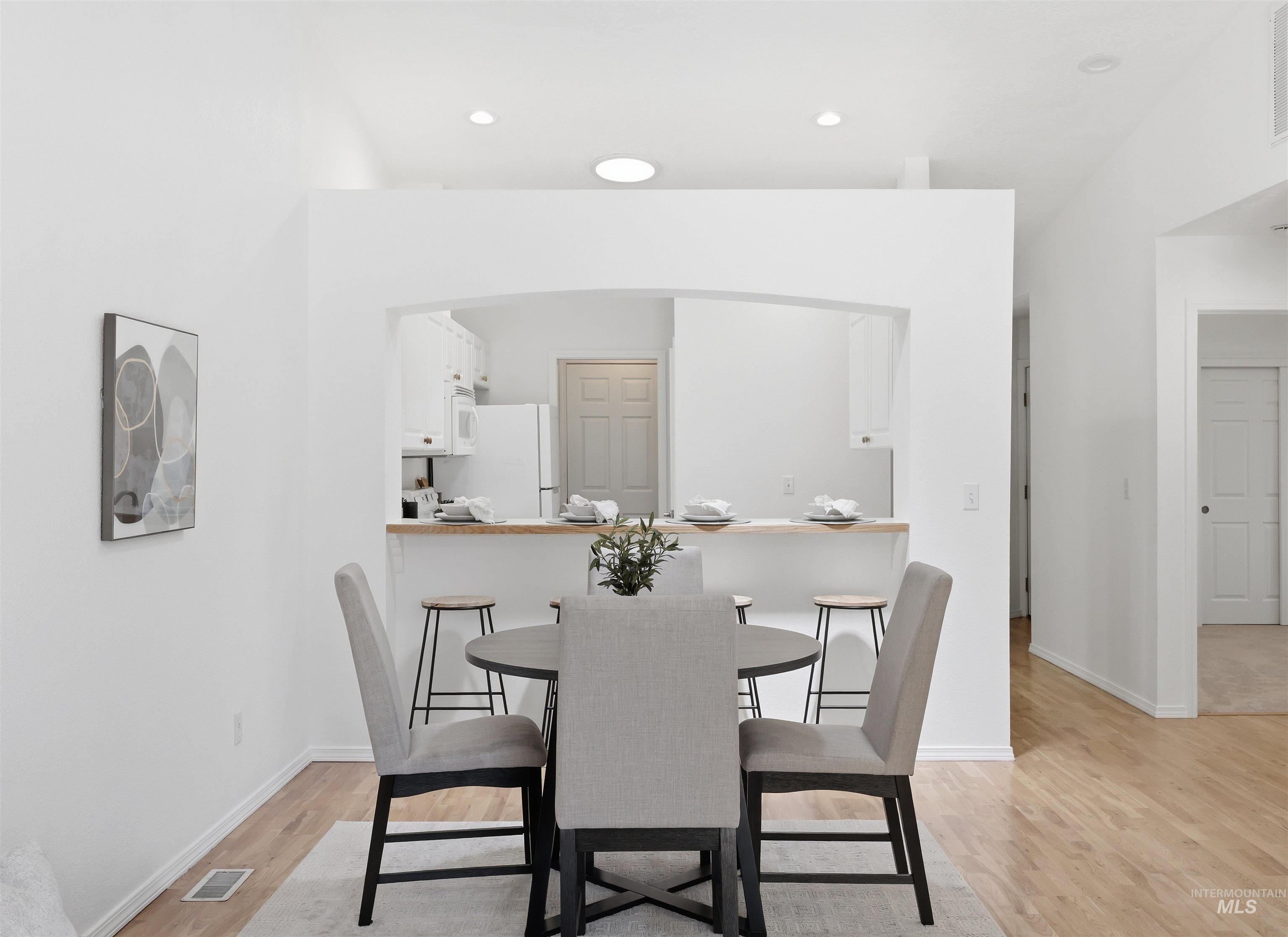 Dining area featuring wood-finish flooring, white walls, and an arched pass-through to the kitchen