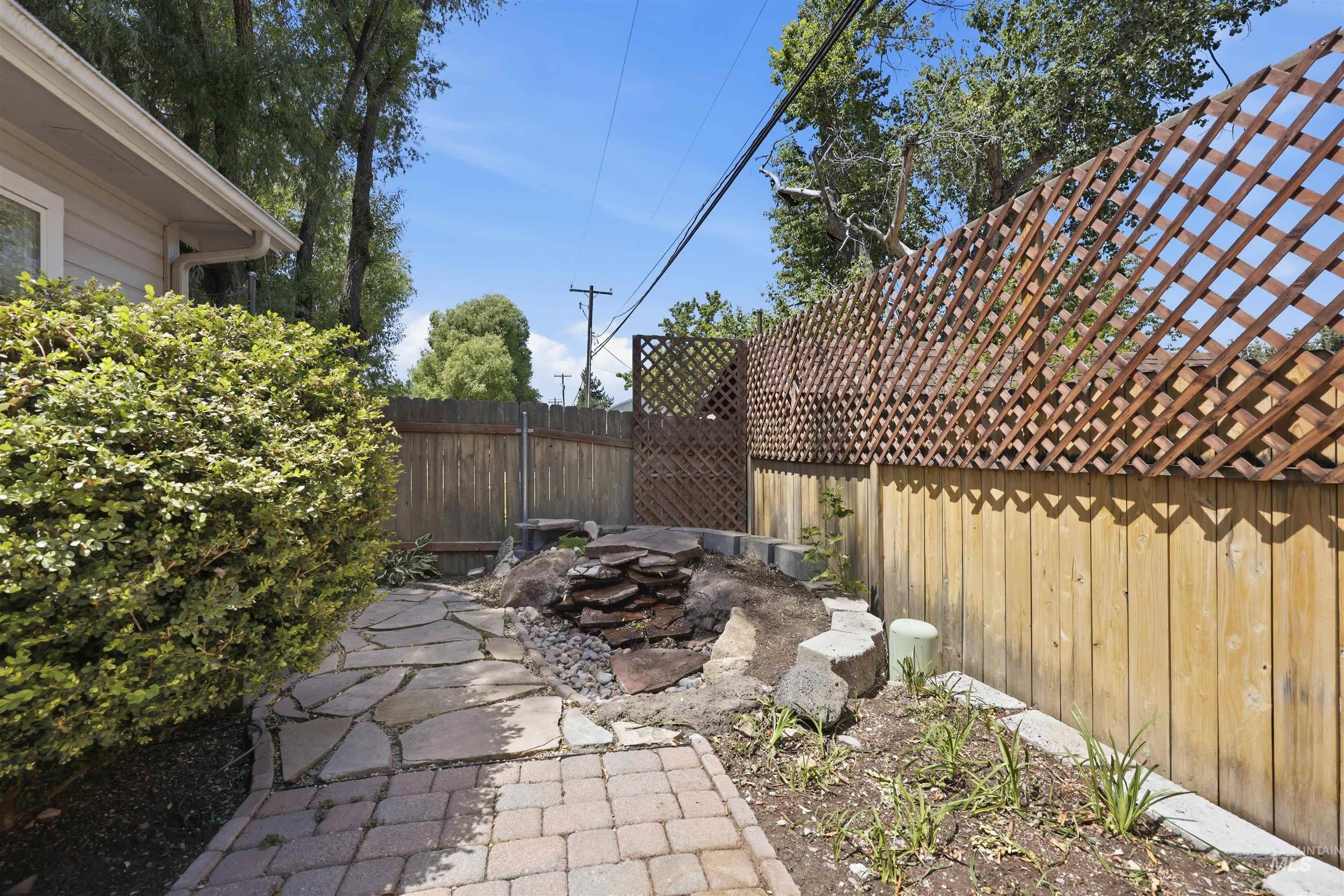 Side yard featuring a paver and flagstone pathway, wood privacy fencing with lattice top, stone landscaping, and established shrubbery