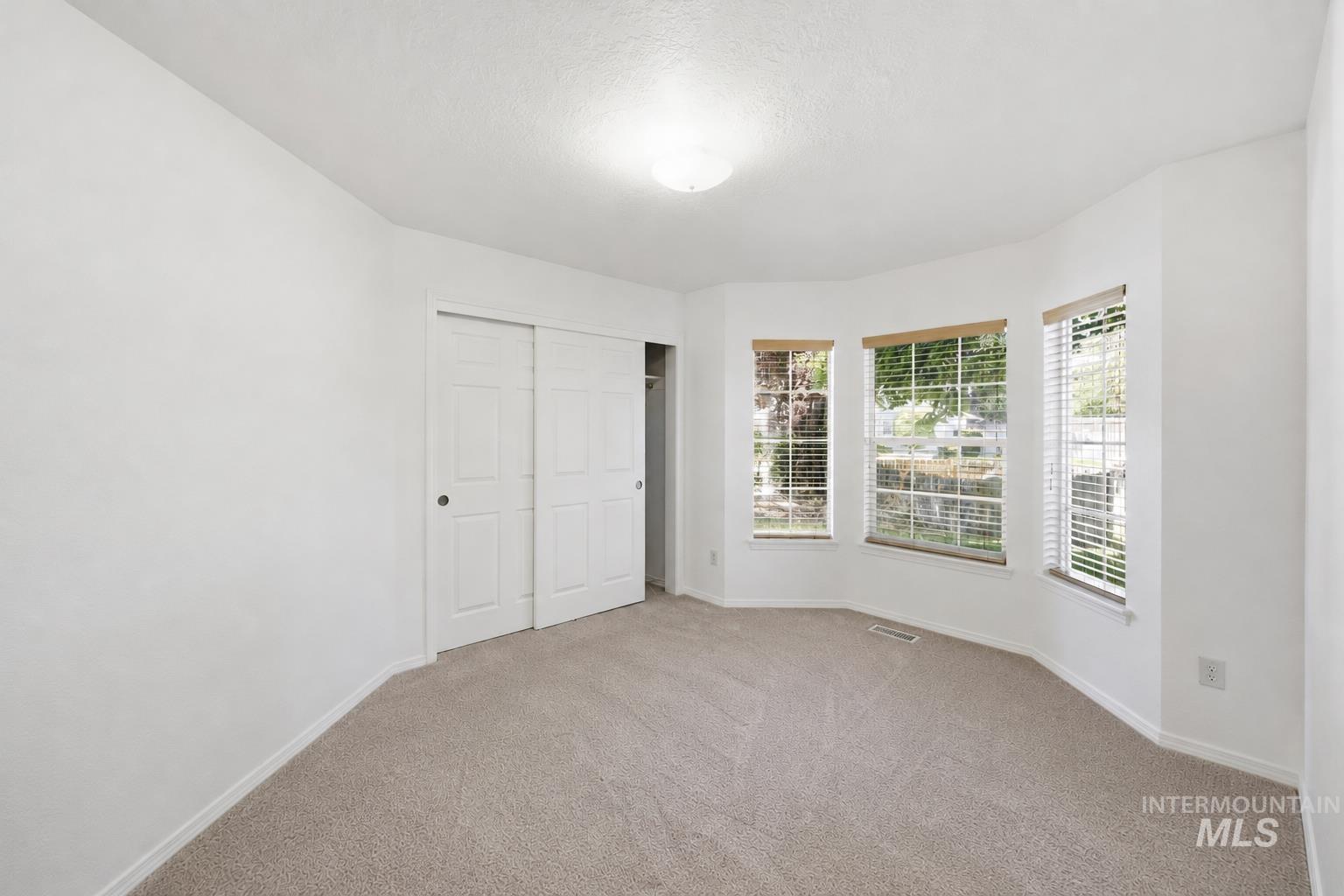 Bright interior space featuring a bay window with three individual panes, plush carpeting, and light-colored walls