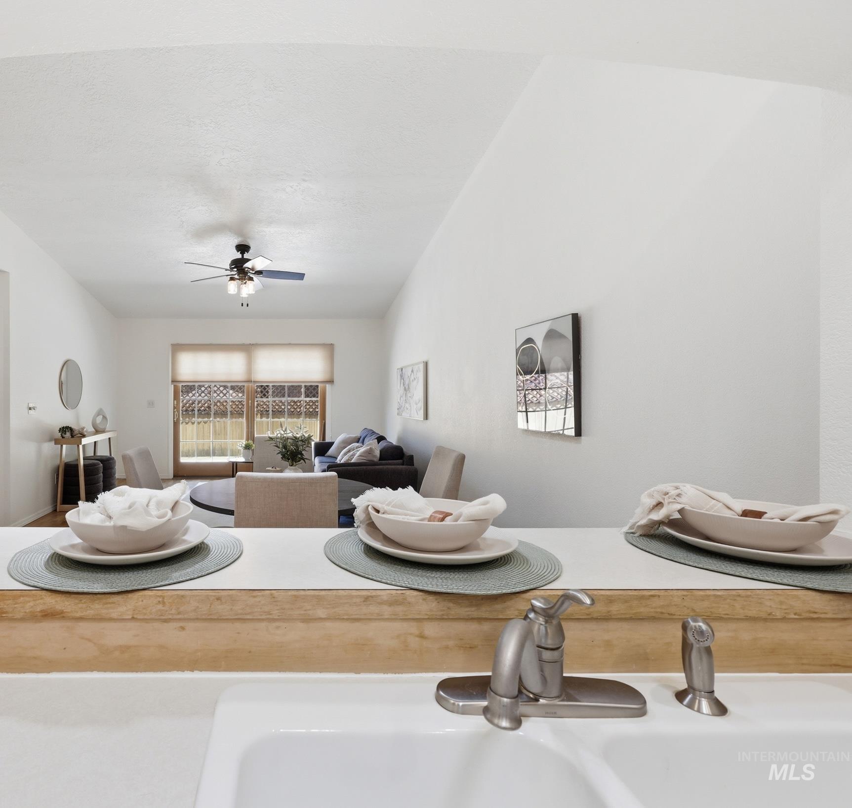 Open-concept living space featuring a vaulted ceiling with a ceiling fan, a window overlooking the backyard, and a white kitchen sink with a brushed nickel faucet