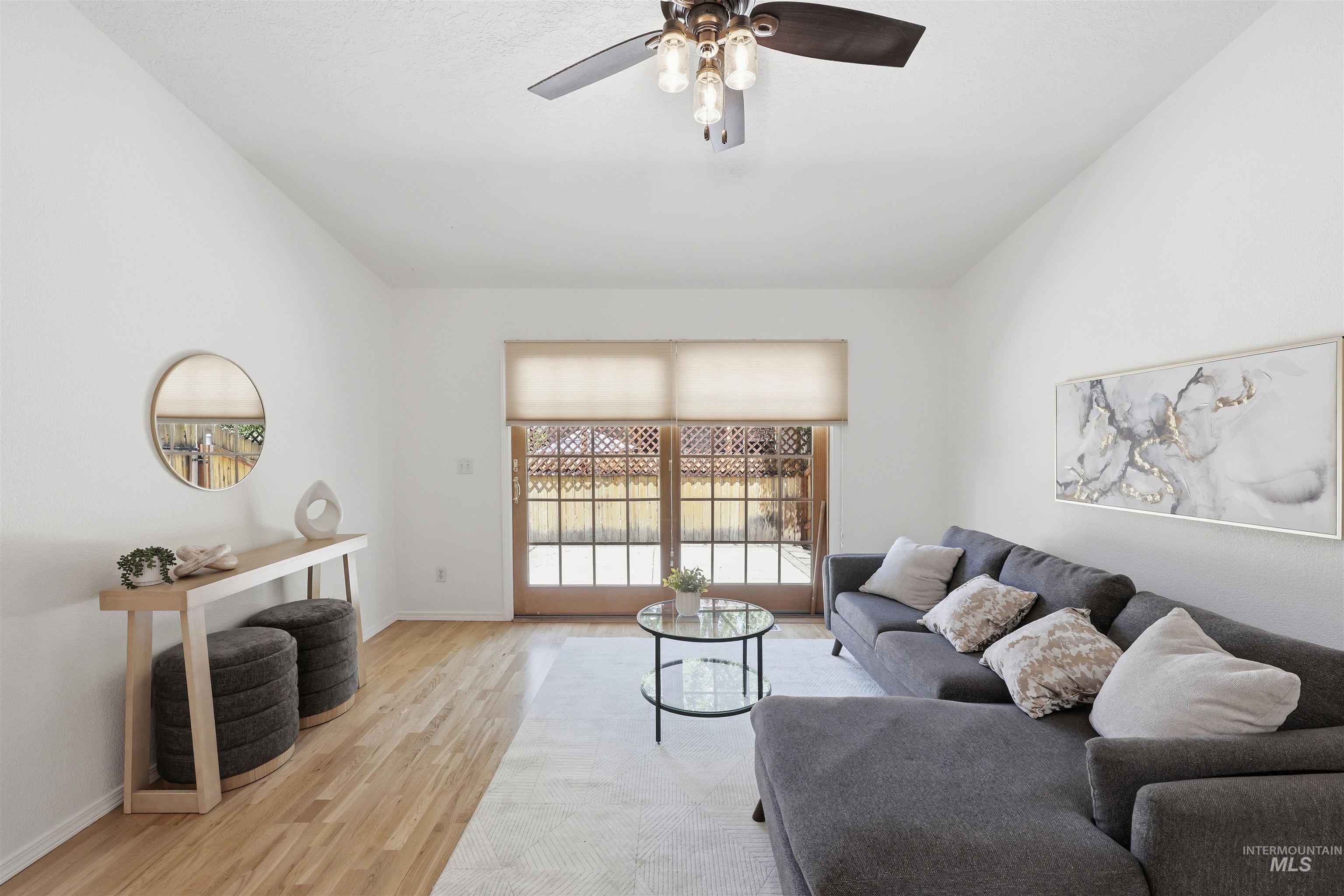 Bright living area featuring wood-finish flooring, vaulted ceilings, a ceiling fan with integrated lighting, and French patio doors with transom windows