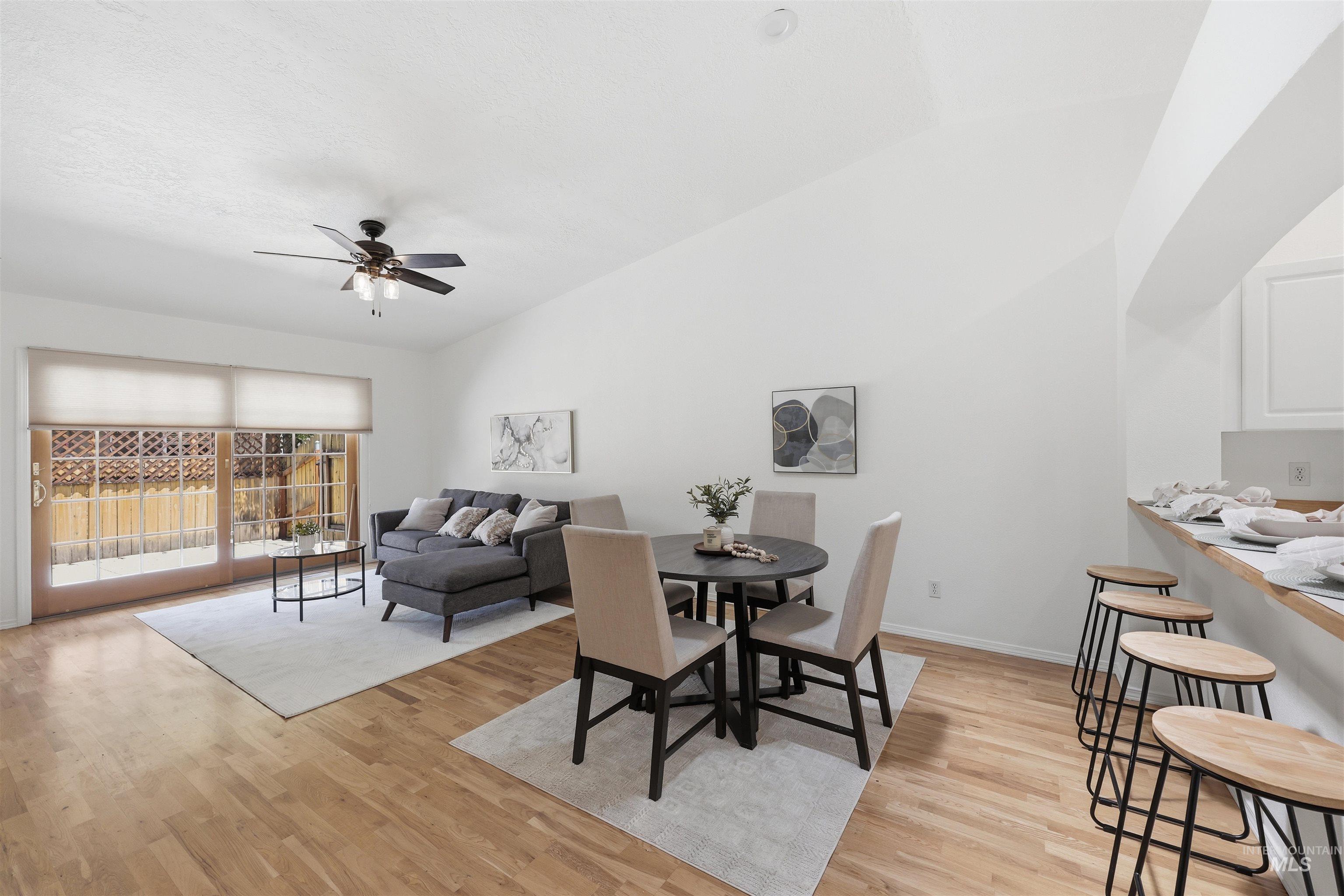 Open-concept living and dining area featuring wood-finish flooring, vaulted ceilings, and a ceiling fan