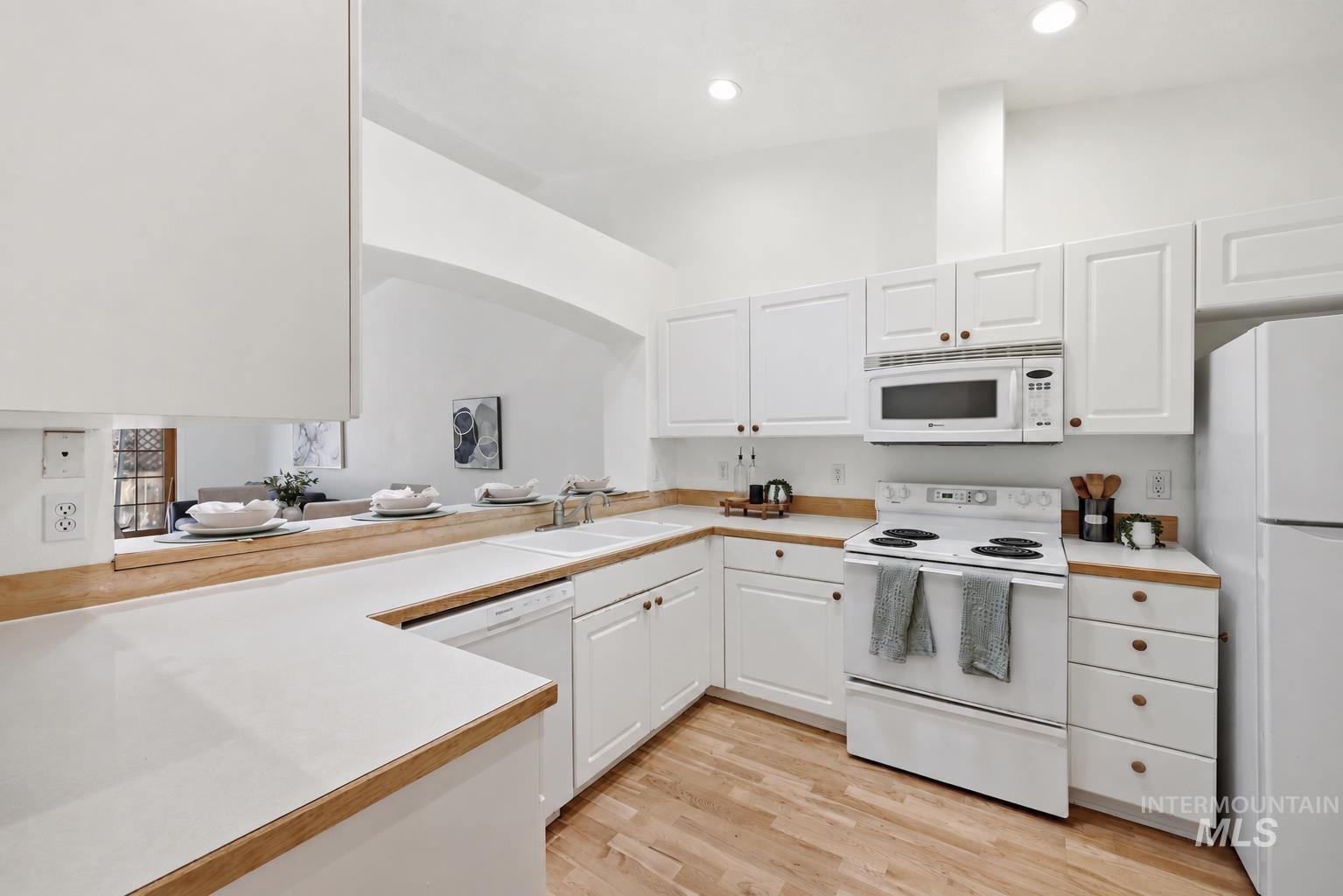 Bright kitchen featuring white cabinetry, wood-finish countertops, wood-finish flooring, and white appliances including a refrigerator, range, microwave, and dishwasher