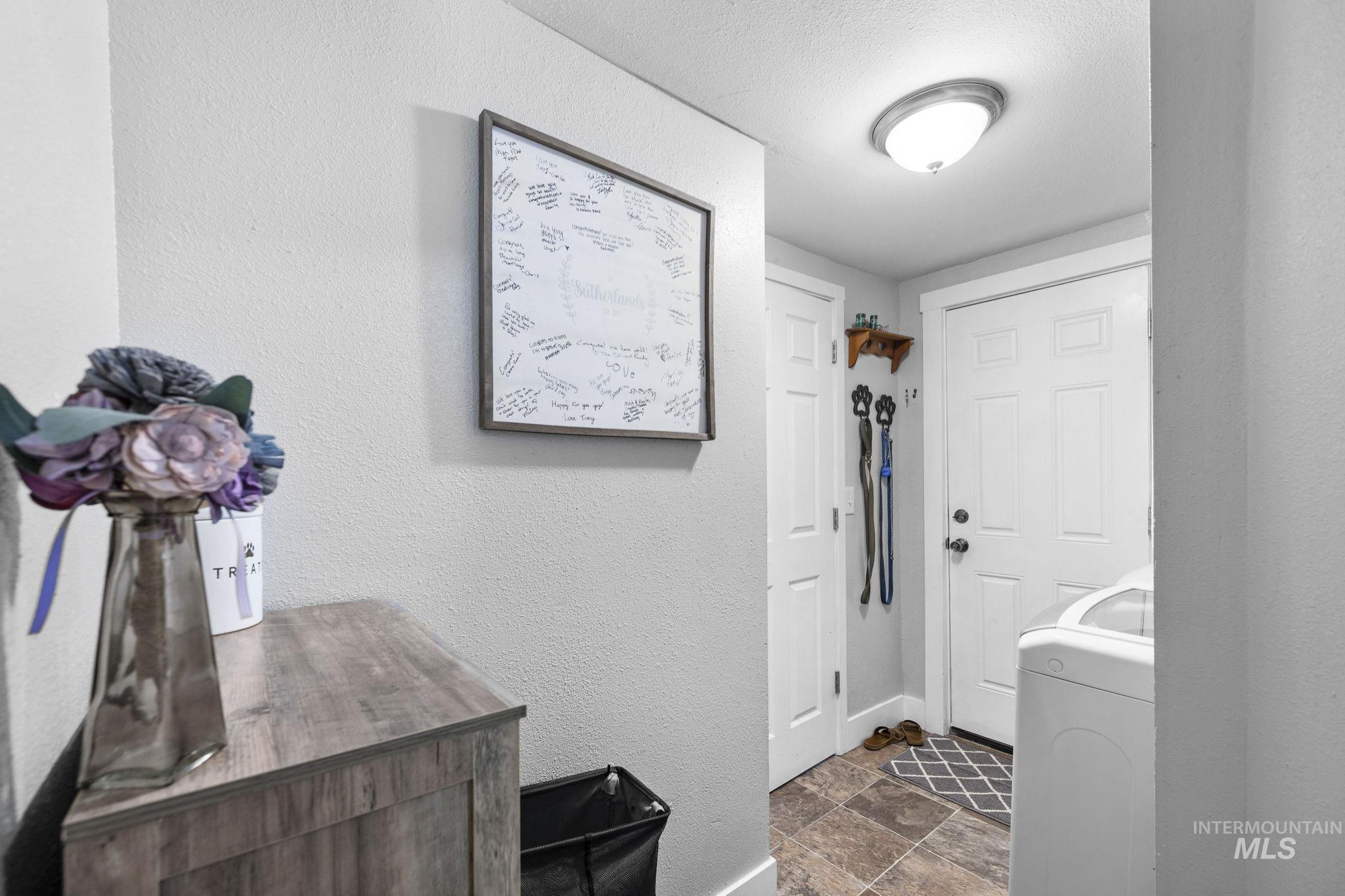 Washroom with a textured wall, washer / clothes dryer, dark stone finish floors, and a textured ceiling
