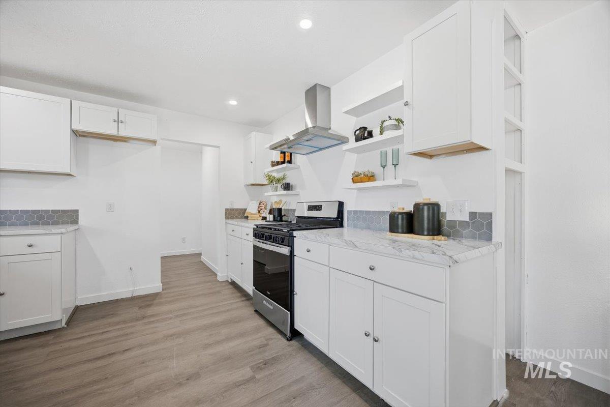 Kitchen with open shelves, stainless steel gas range oven, white cabinetry, wall chimney exhaust hood, and recessed lighting