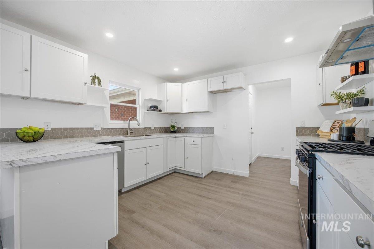Kitchen featuring open shelves, black gas range oven, wall chimney range hood, white cabinets, and light countertops