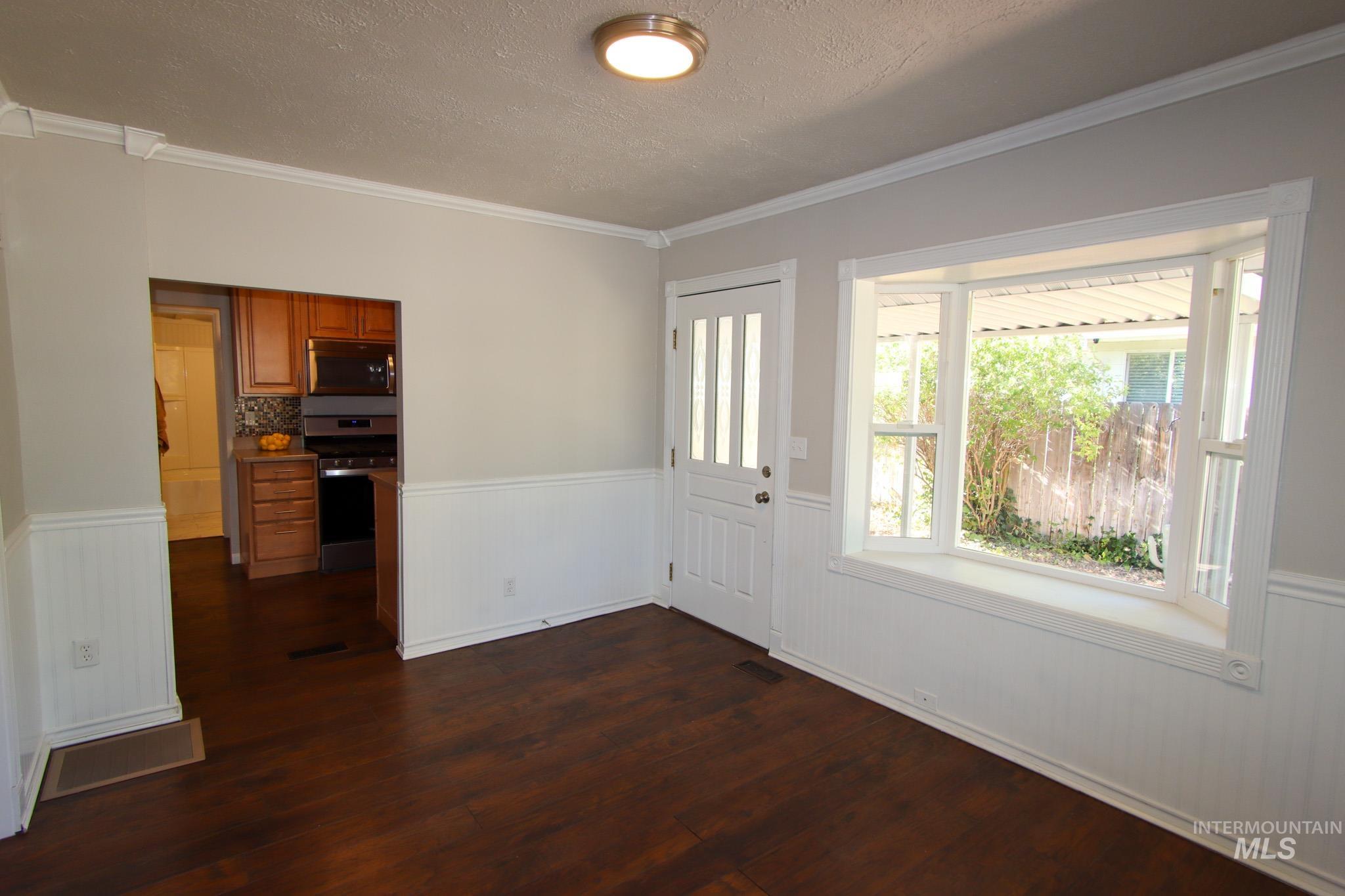 Entrance foyer featuring wainscoting, crown molding, dark wood-style floors, and a textured ceiling