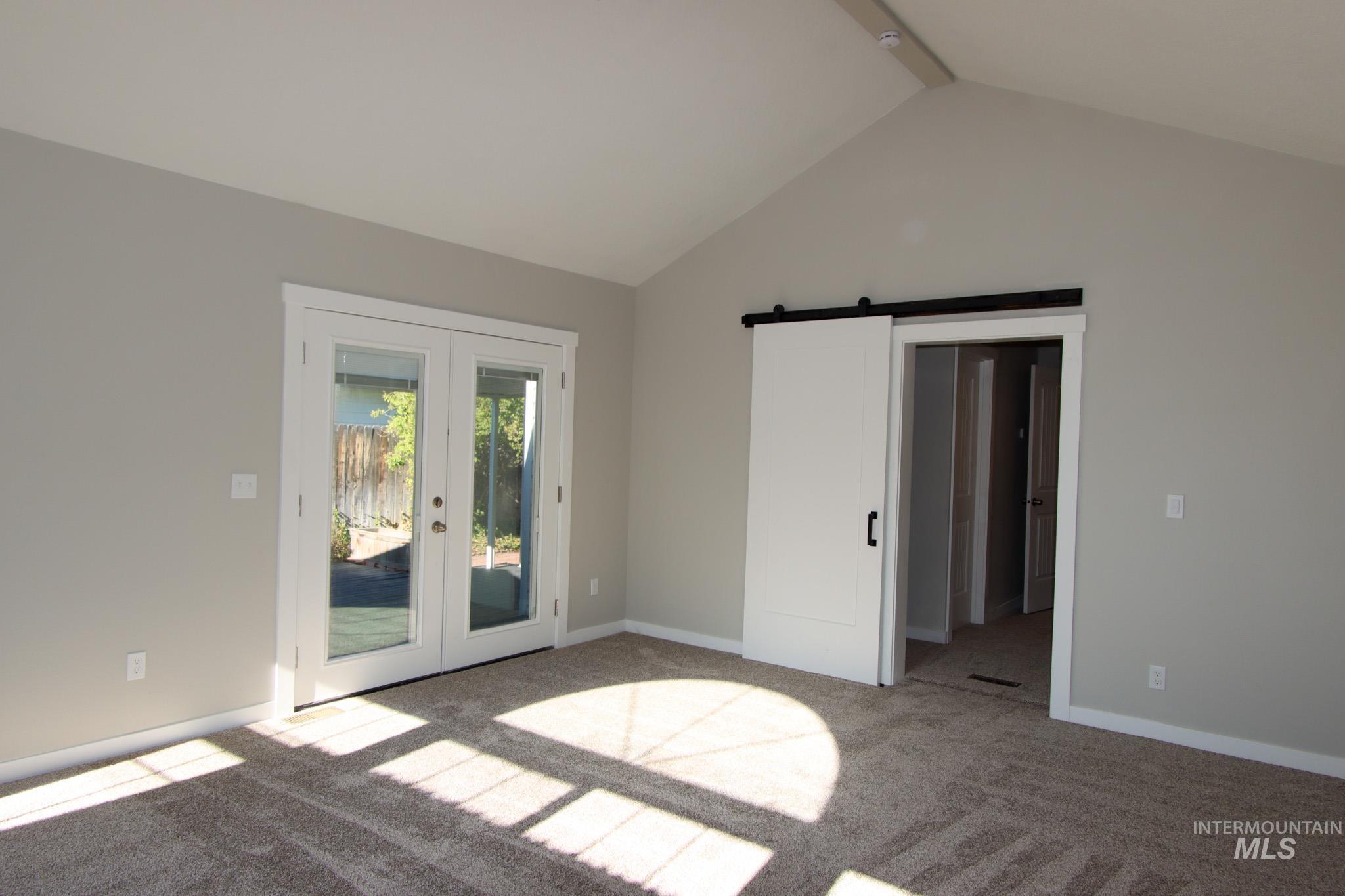 Unfurnished bedroom featuring a barn door, beamed ceiling, carpet flooring, french doors, and access to exterior