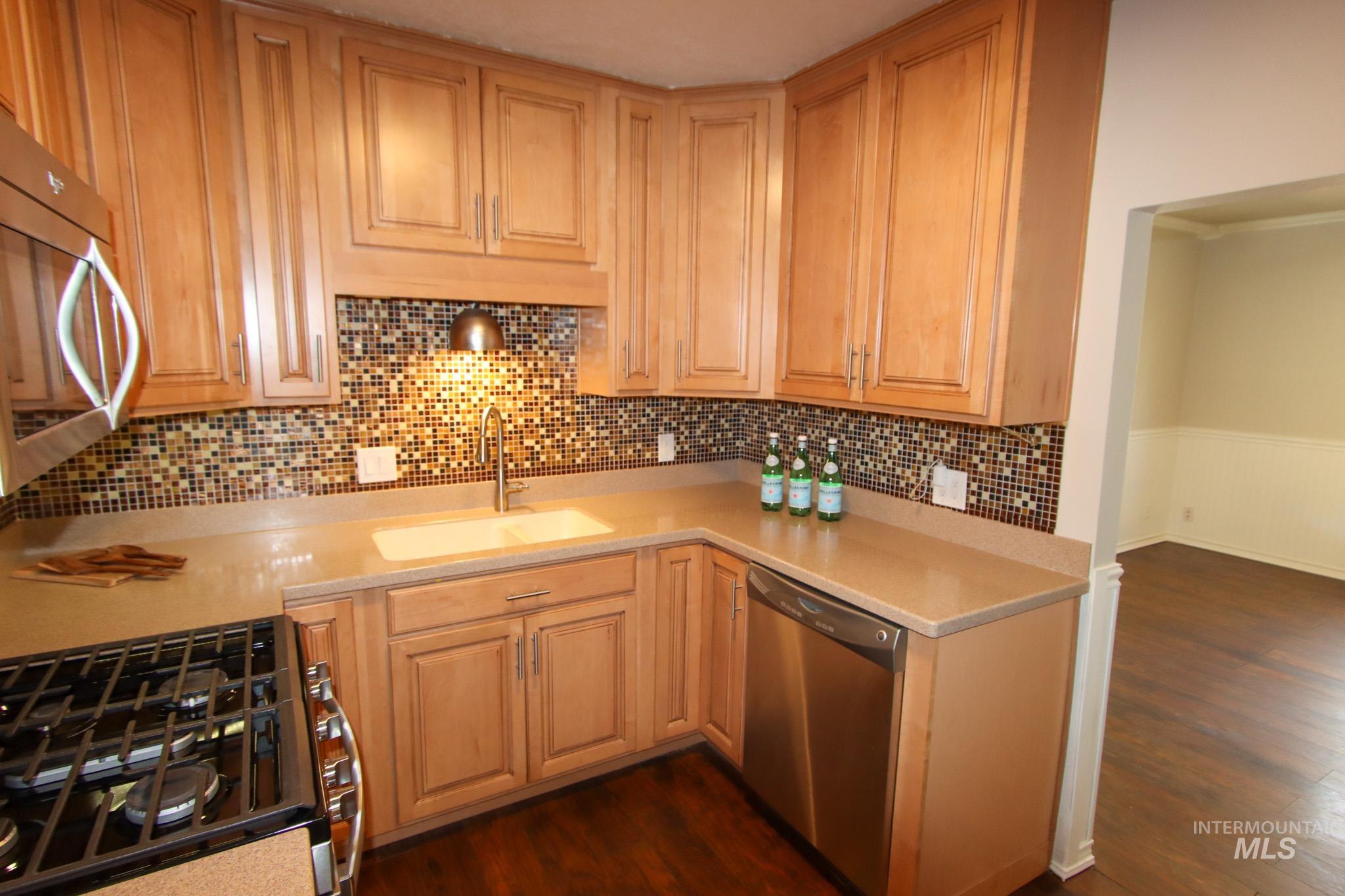 Kitchen featuring stainless steel appliances, dark wood finished floors, decorative backsplash, light brown cabinetry, and light stone countertops