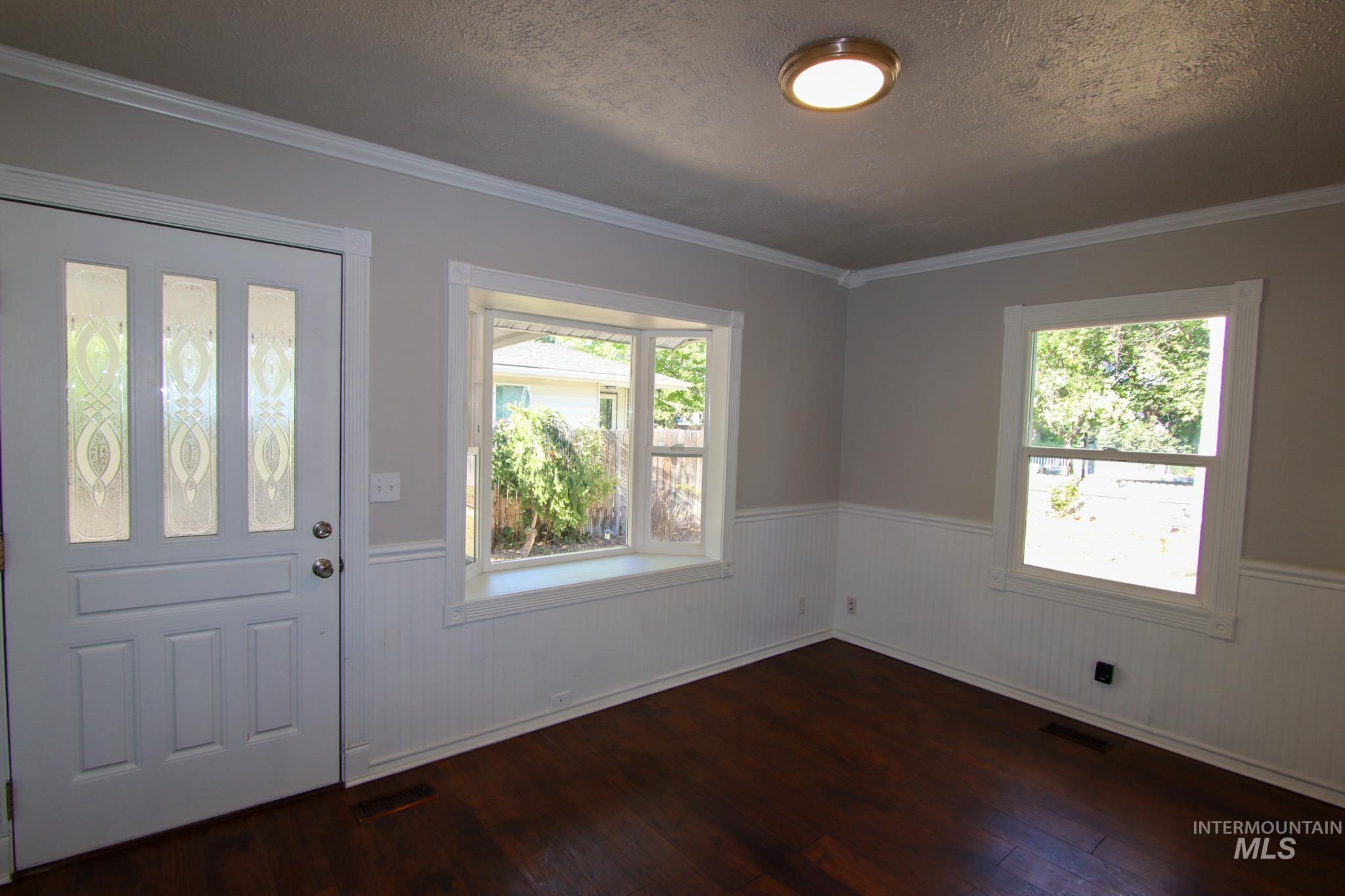 Foyer with a wainscoted wall, dark wood-type flooring, ornamental molding, a textured ceiling, and plenty of natural light