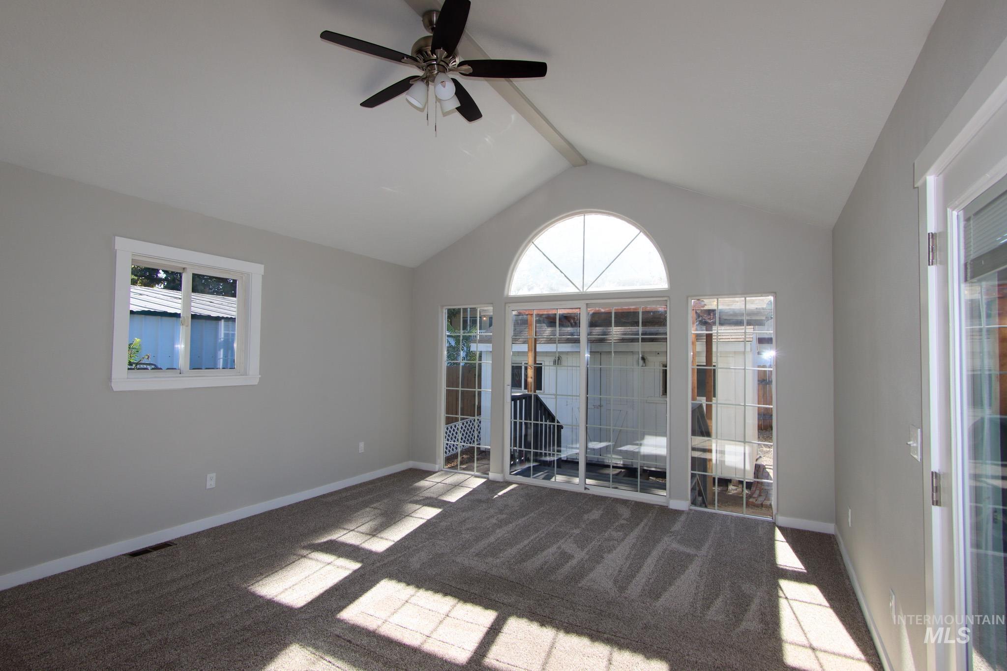 Carpeted spare room featuring vaulted ceiling and a ceiling fan