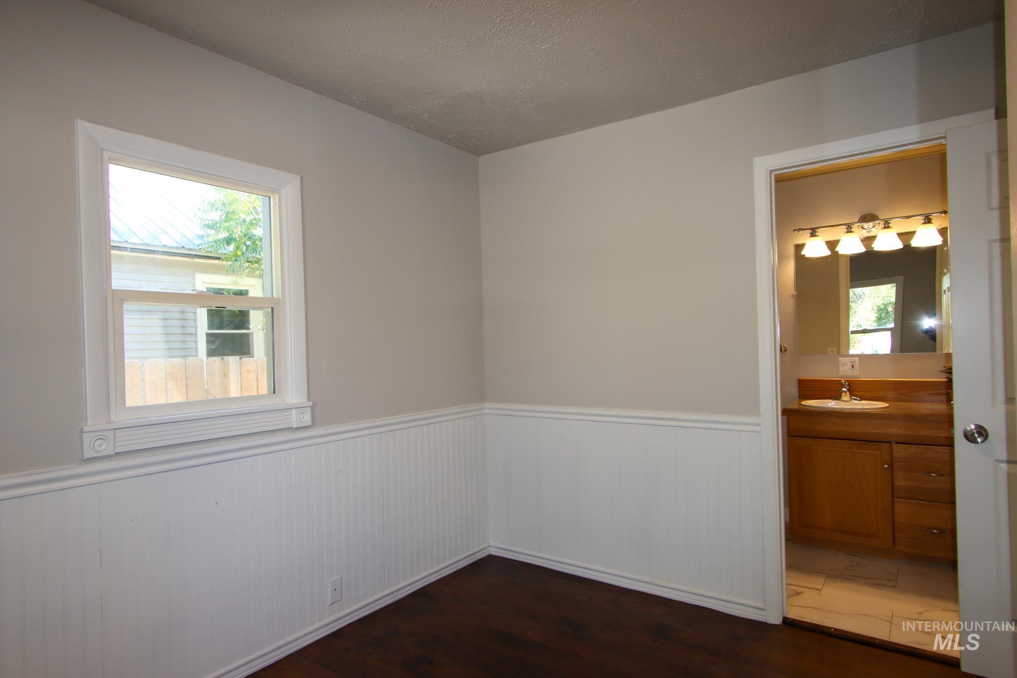 Unfurnished room featuring a wainscoted wall and dark wood-style floors