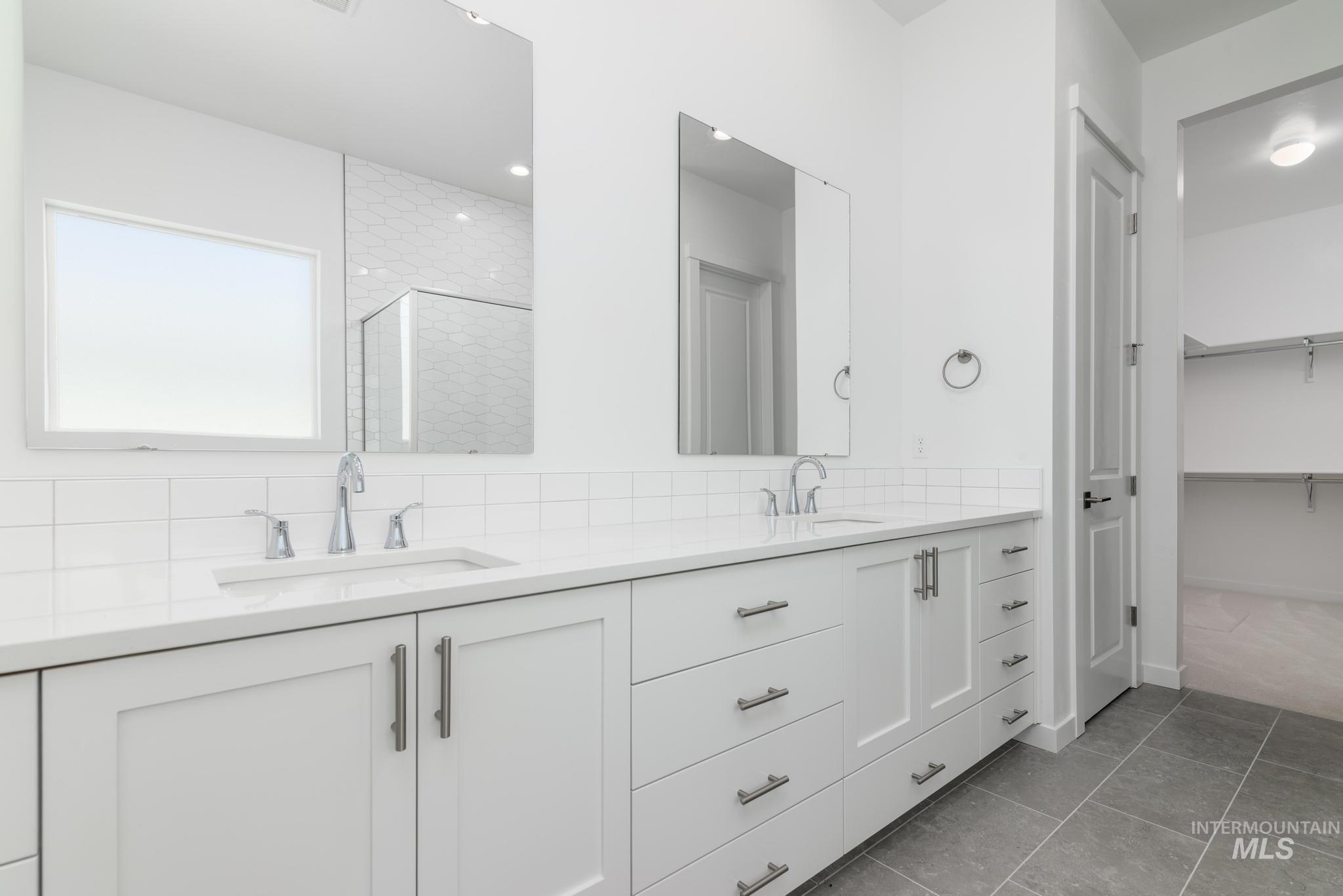 Bathroom featuring a stall shower, double vanity, tasteful backsplash, light tile patterned flooring, and a walk in closet
