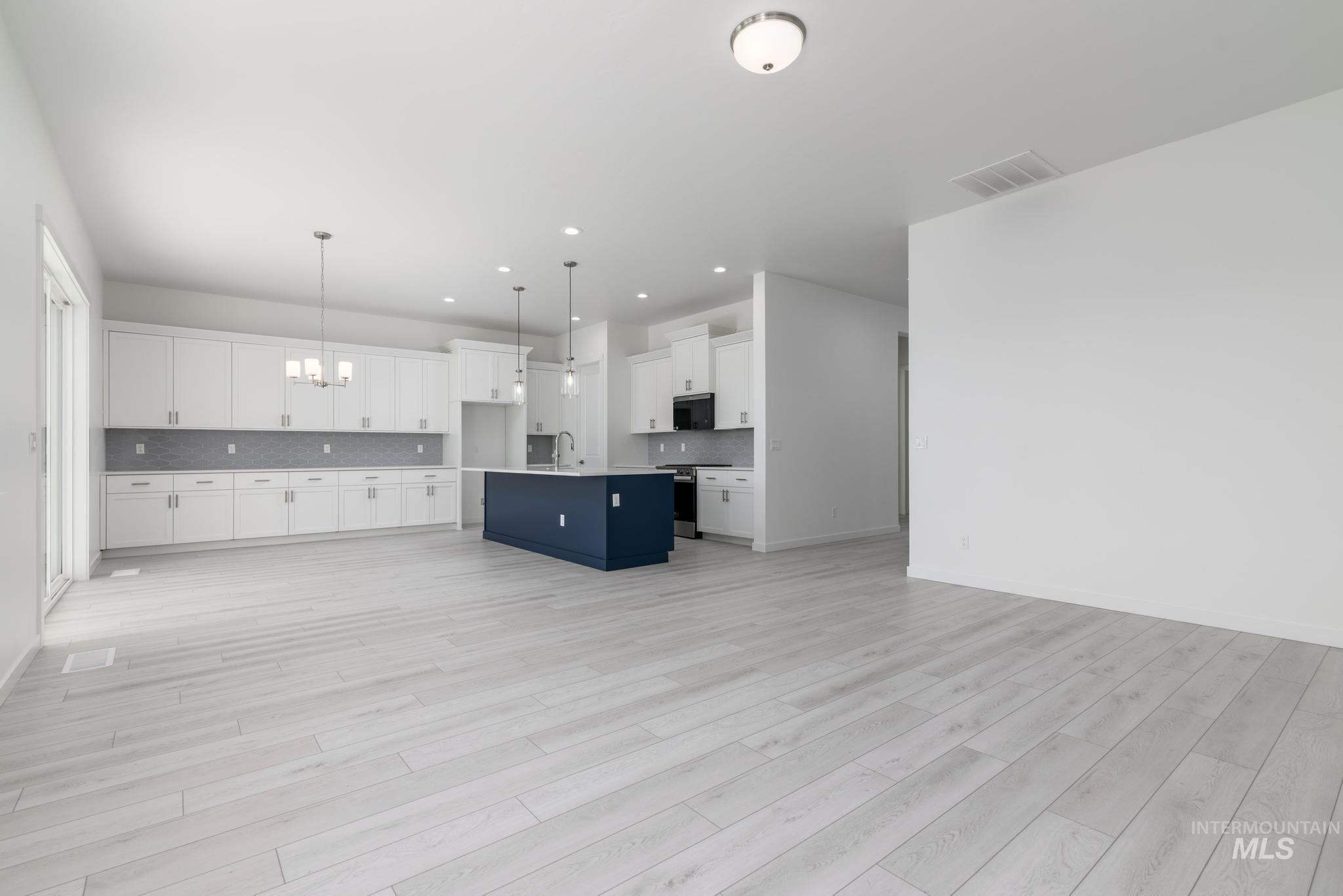 Kitchen featuring open floor plan, white cabinets, a chandelier, an island with sink, and decorative backsplash