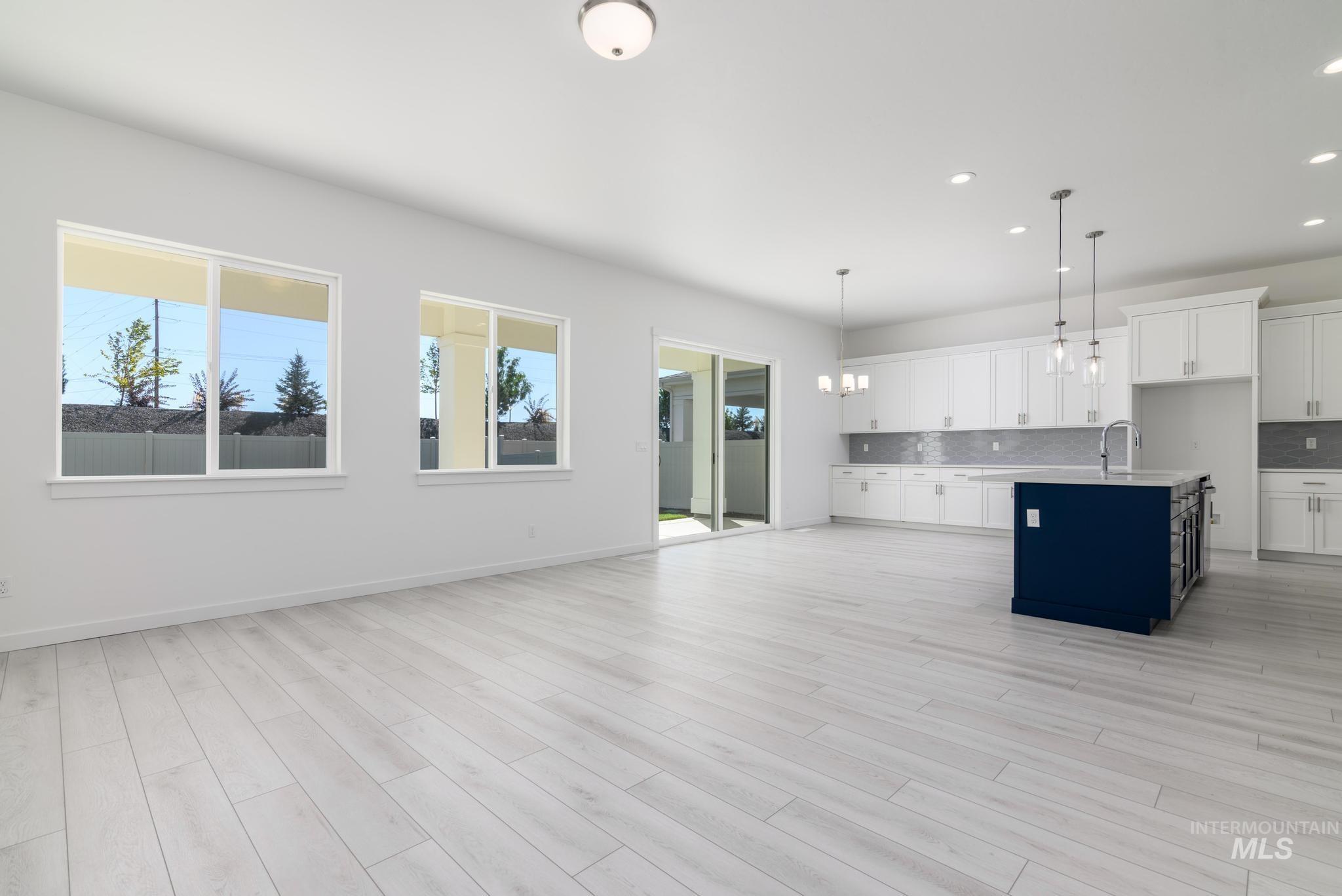 Kitchen featuring white cabinets, a center island with sink, hanging light fixtures, backsplash, and open floor plan