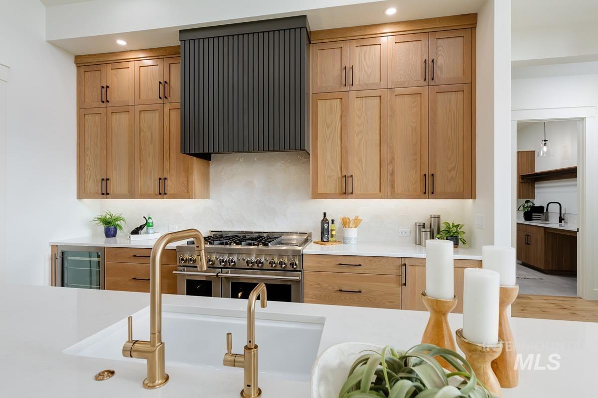 Kitchen with range with two ovens, exhaust hood, wine cooler, tasteful backsplash, and light stone counters