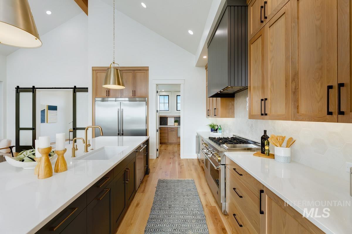 Kitchen featuring high vaulted ceiling, a barn door, light wood finished floors, premium appliances, and hanging light fixtures