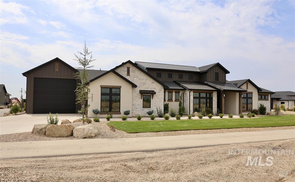 Modern farmhouse style home featuring driveway, a metal roof, stone siding, a front lawn, and board and batten siding