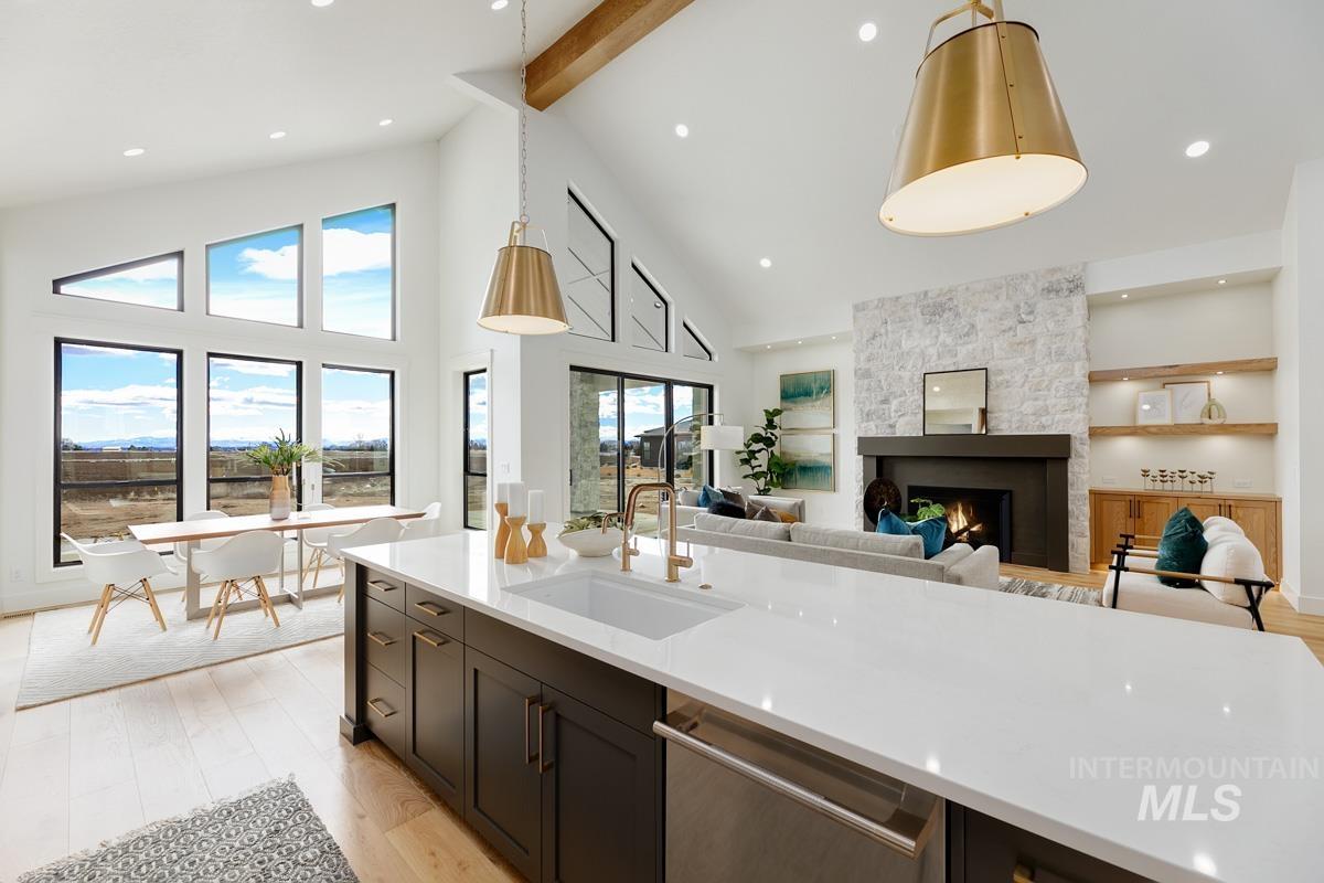 Kitchen featuring light wood finished floors, high vaulted ceiling, stainless steel dishwasher, light stone counters, and open floor plan