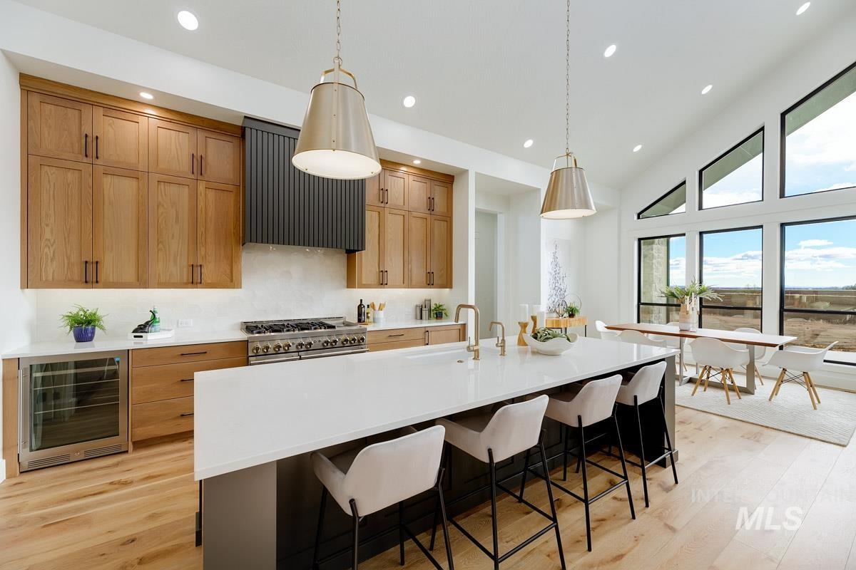 Kitchen featuring decorative light fixtures, an island with sink, decorative backsplash, a kitchen breakfast bar, and wine cooler