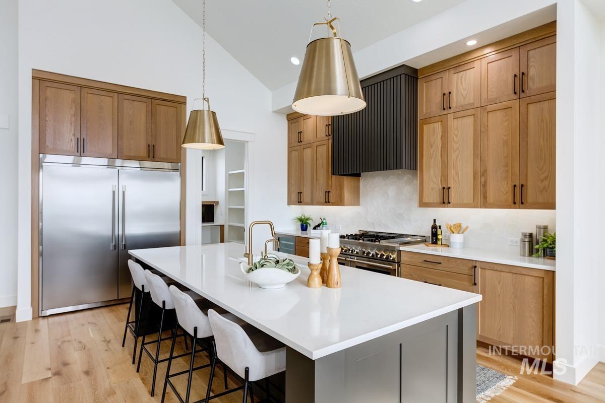 Kitchen with premium appliances, an island with sink, light wood-style floors, pendant lighting, and a breakfast bar area