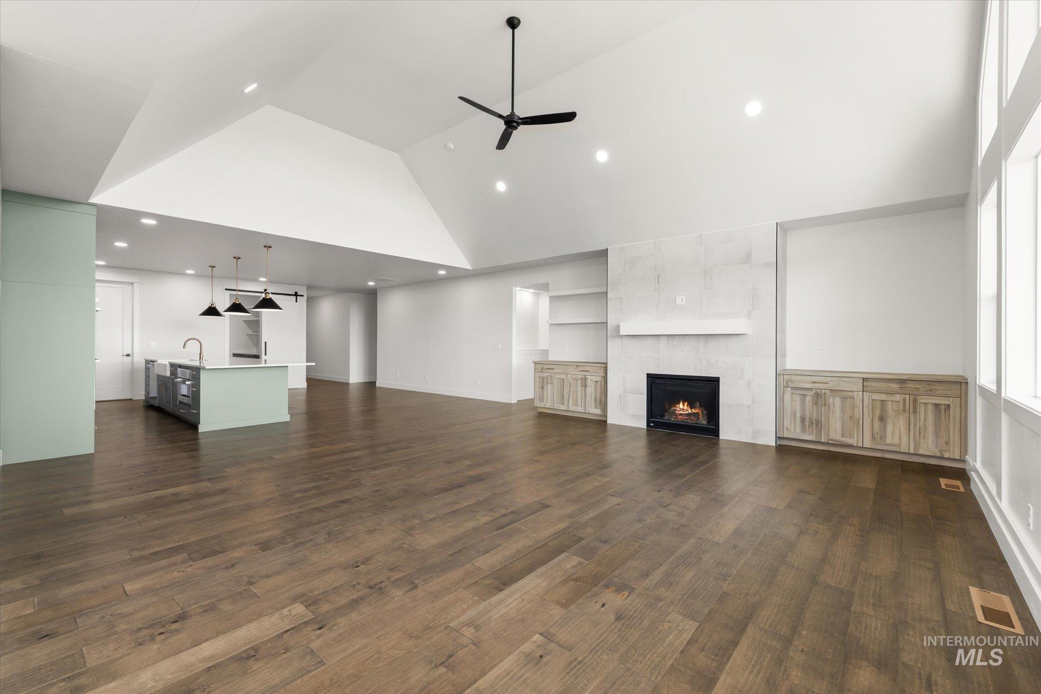 Unfurnished living room featuring high vaulted ceiling, a tiled fireplace, ceiling fan, dark wood-style floors, and recessed lighting