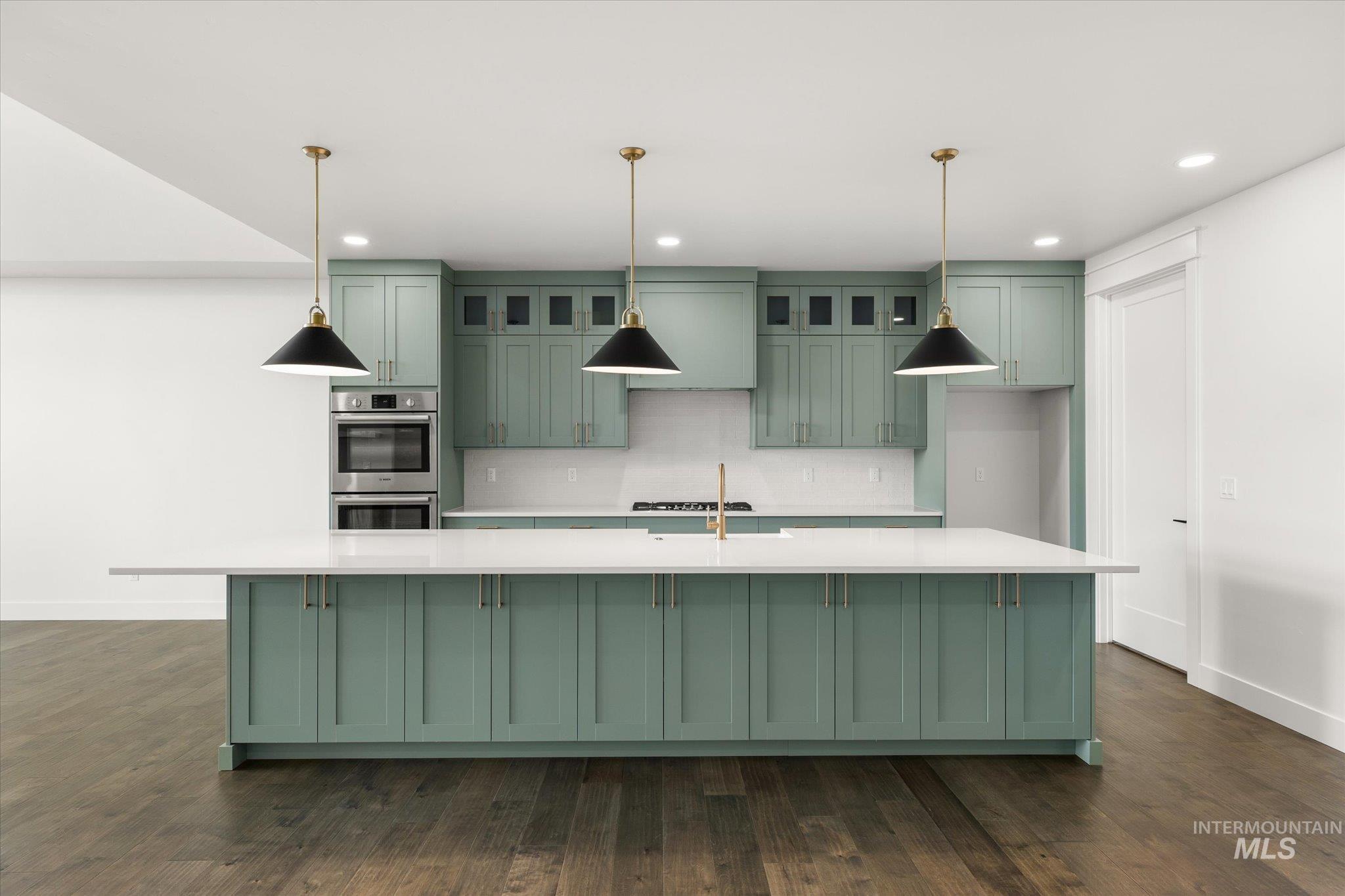 Kitchen featuring green cabinetry, a large island, stainless steel appliances, dark wood-style floors, and decorative light fixtures