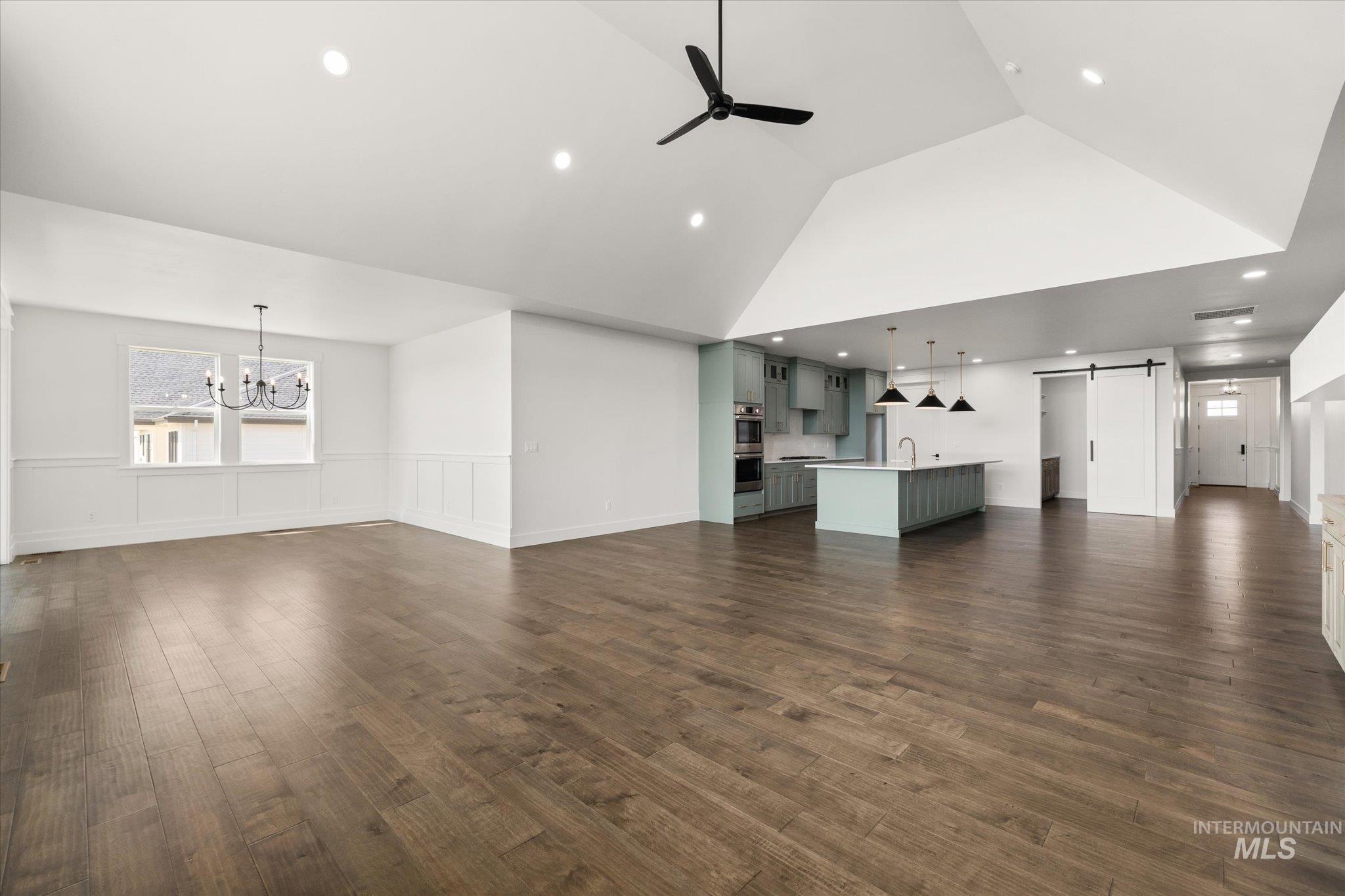 Unfurnished living room with a barn door, ceiling fan, dark wood-style floors, recessed lighting, and a wainscoted wall