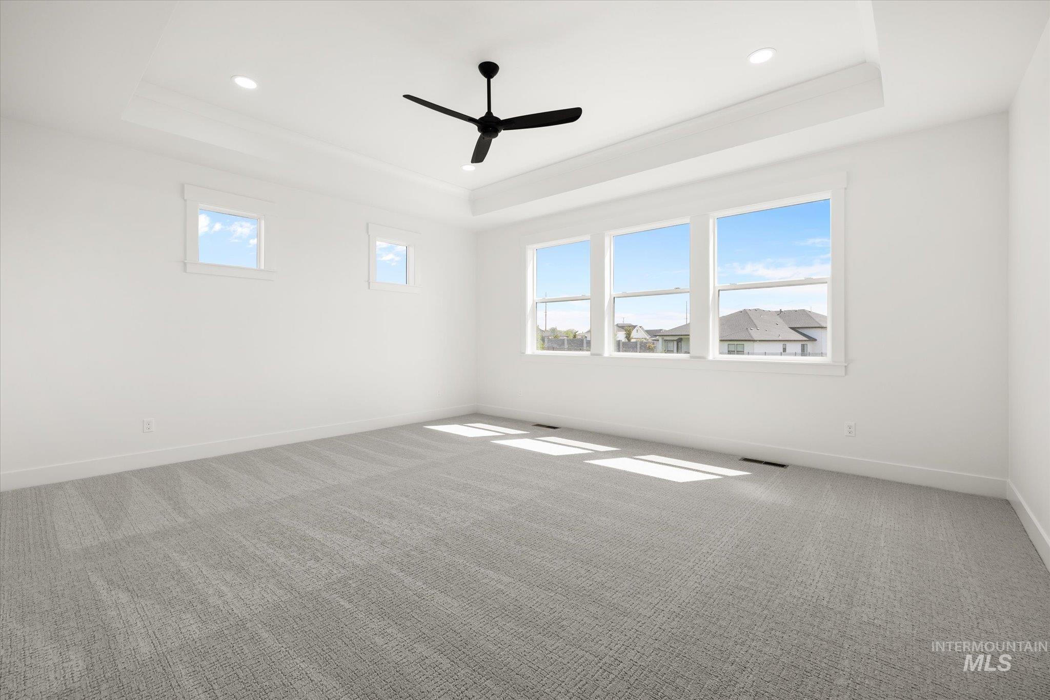 Carpeted bedroom featuring a raised ceiling and ceiling fan