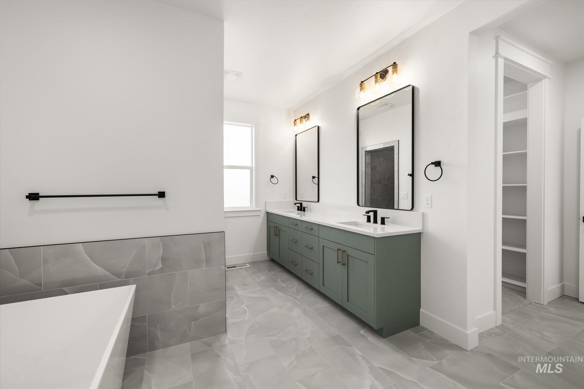 Full bathroom featuring double vanity, a freestanding tub, light marble finish floors, and a walk in closet