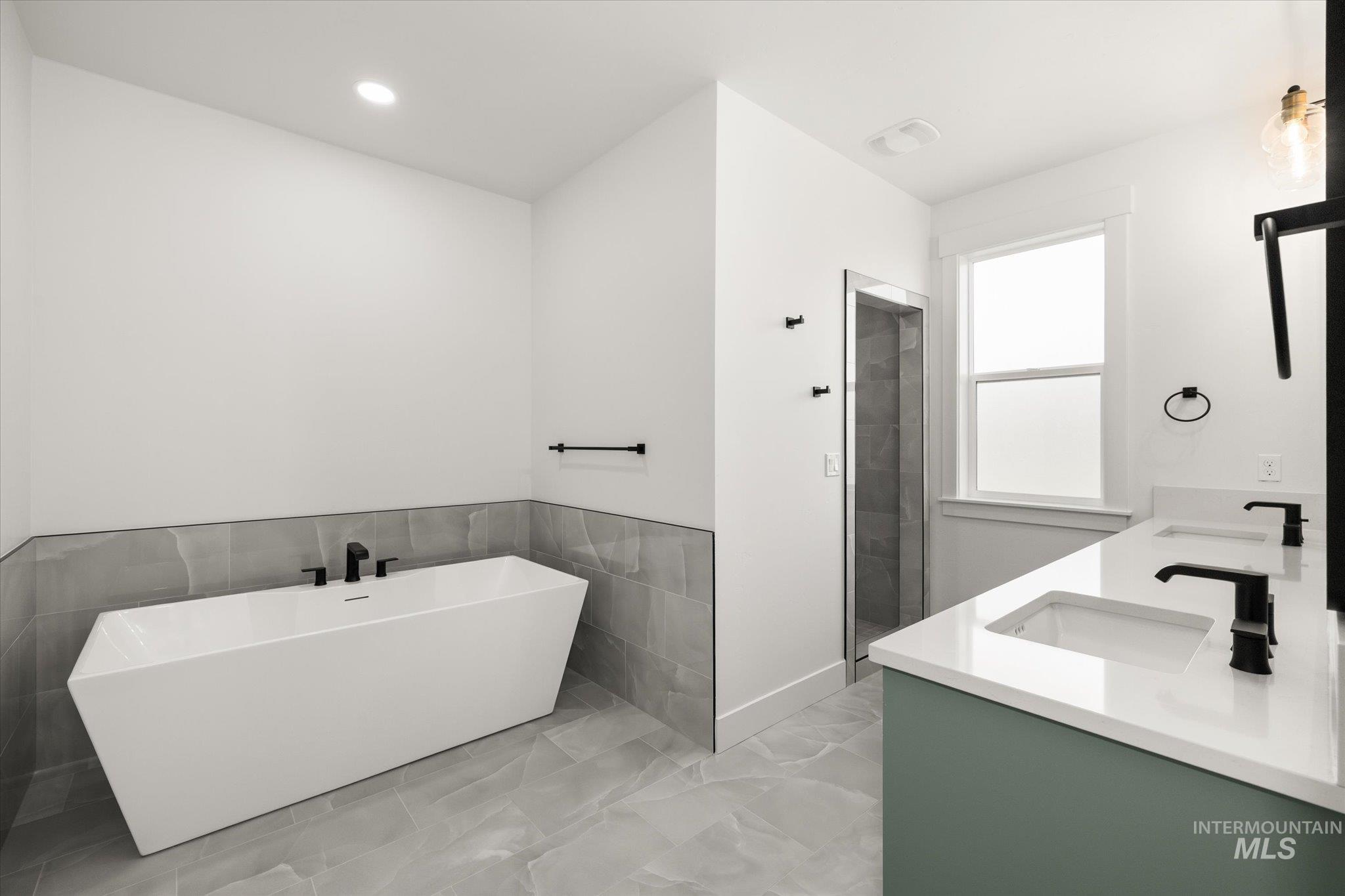 Full bath with a soaking tub, double vanity, light marble finish floors, and recessed lighting