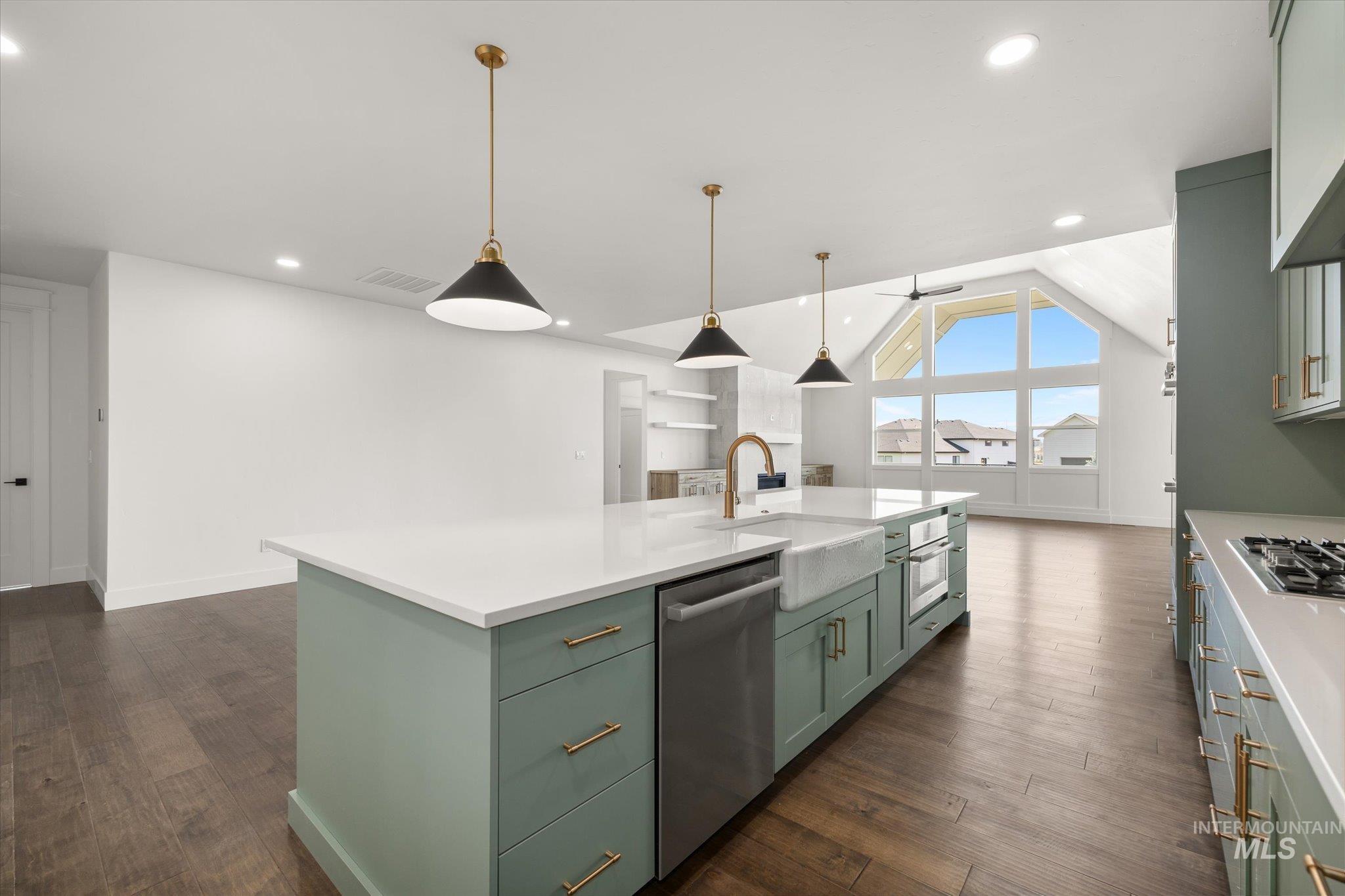 Kitchen featuring green cabinetry, decorative light fixtures, an island with sink, dark wood finished floors, and stainless steel appliances