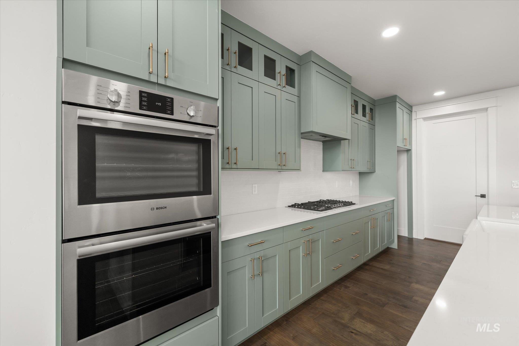 Kitchen featuring appliances with stainless steel finishes, glass insert cabinets, dark wood-style flooring, recessed lighting, and tasteful backsplash