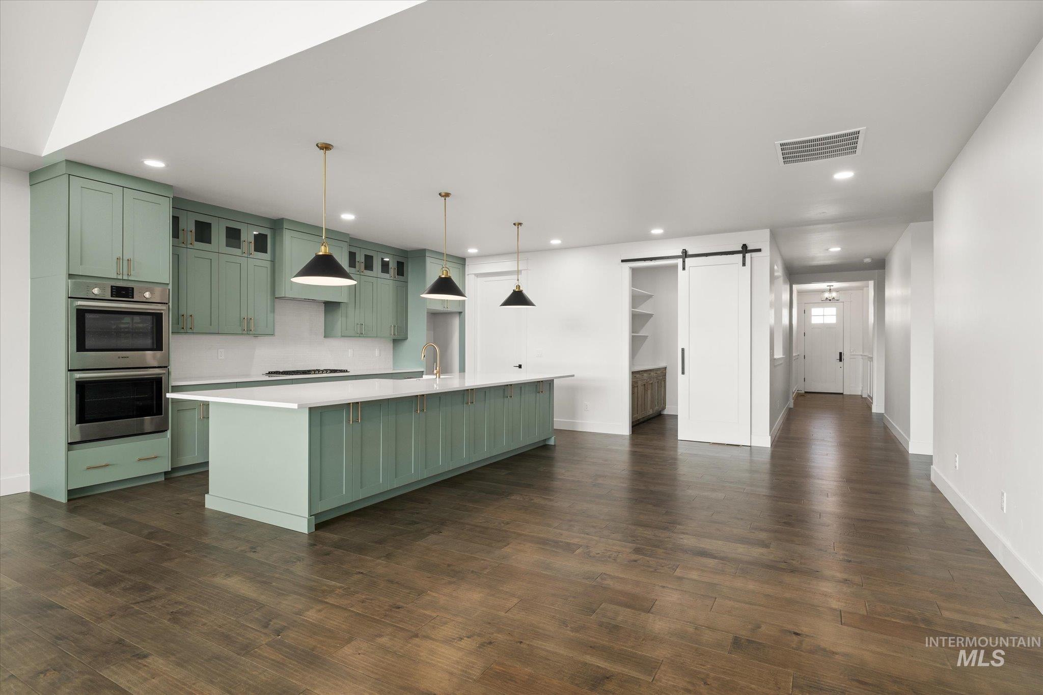Kitchen with green cabinetry, a barn door, glass insert cabinets, stainless steel double oven, and an island with sink