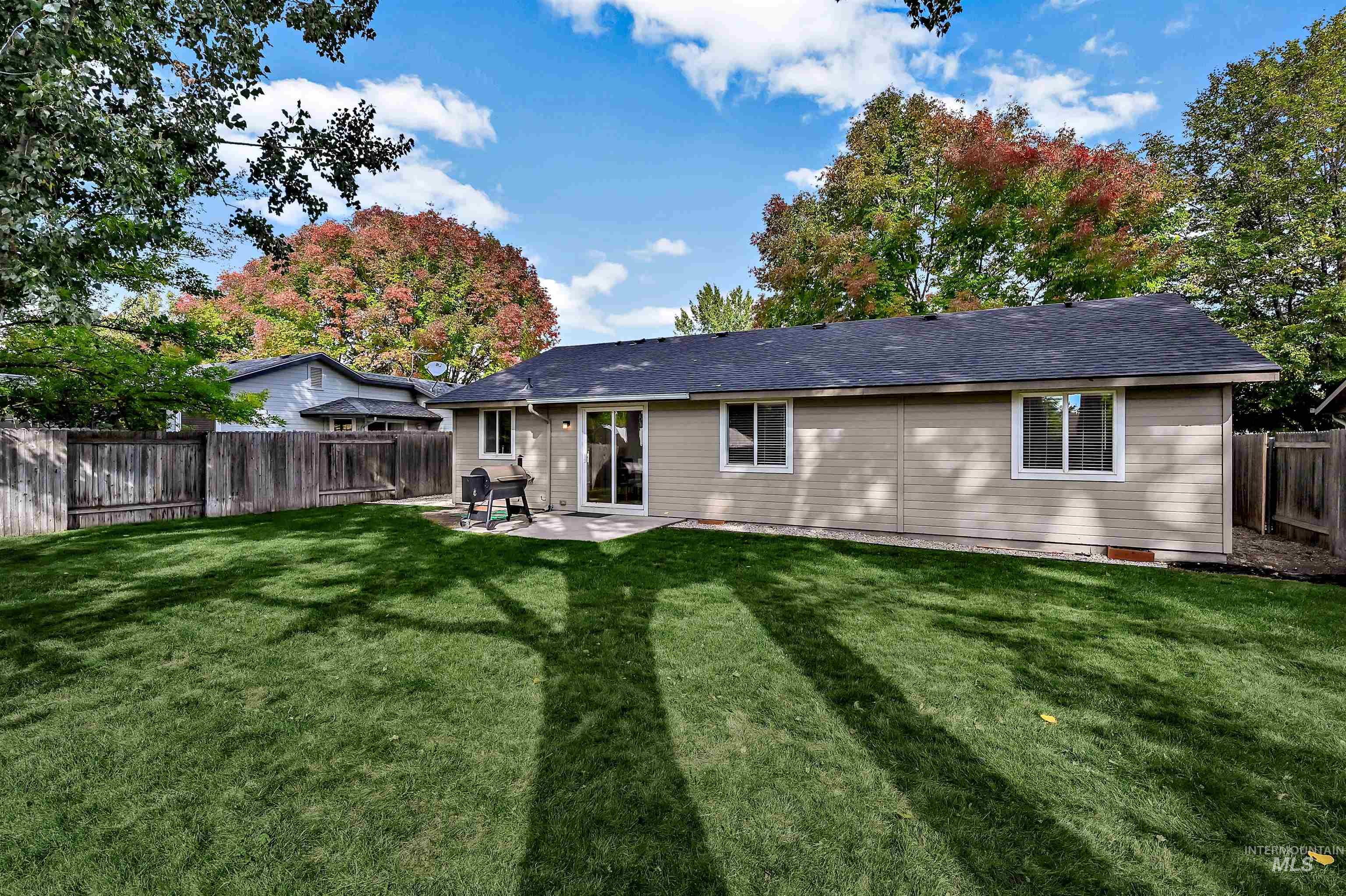 Rear view of property with a concrete patio, gravel area, and a fenced backyard with large trees