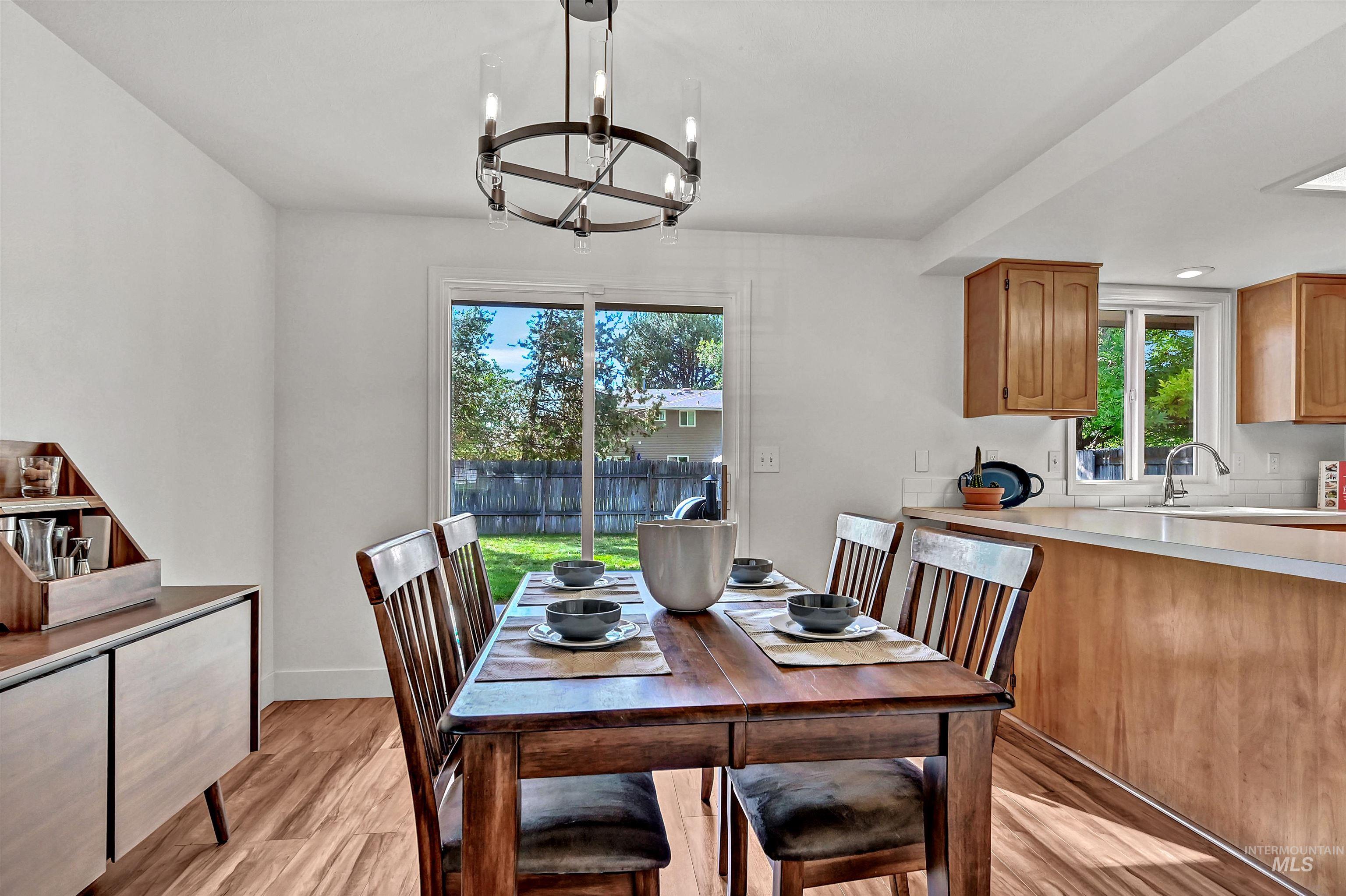 Dining are with light wood-style floors, a chandelier, and recessed lighting + a door to the concrete patio in the large backyard