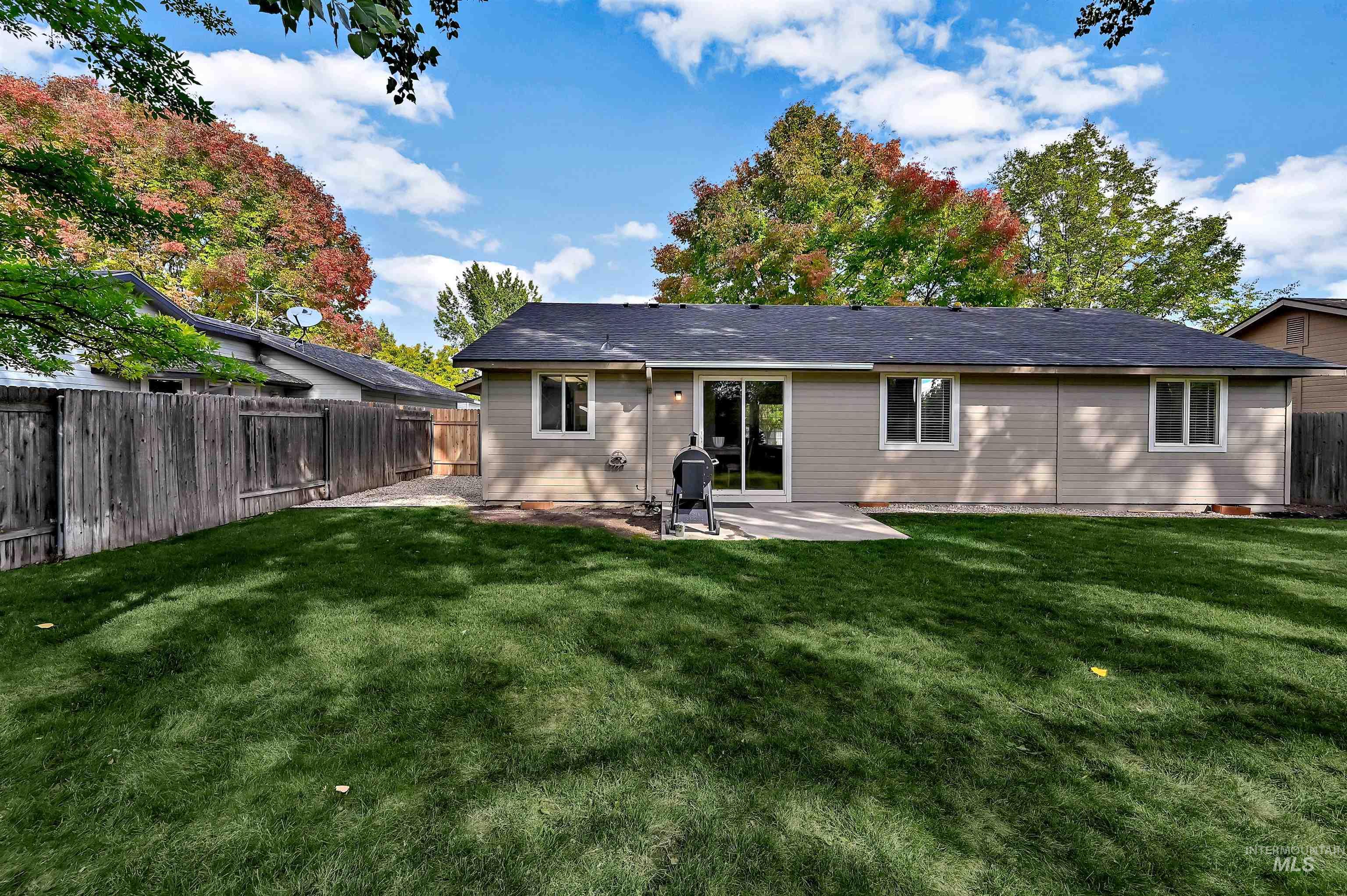 Rear view of property with a concrete patio, gravel area, and a fenced backyard with large trees