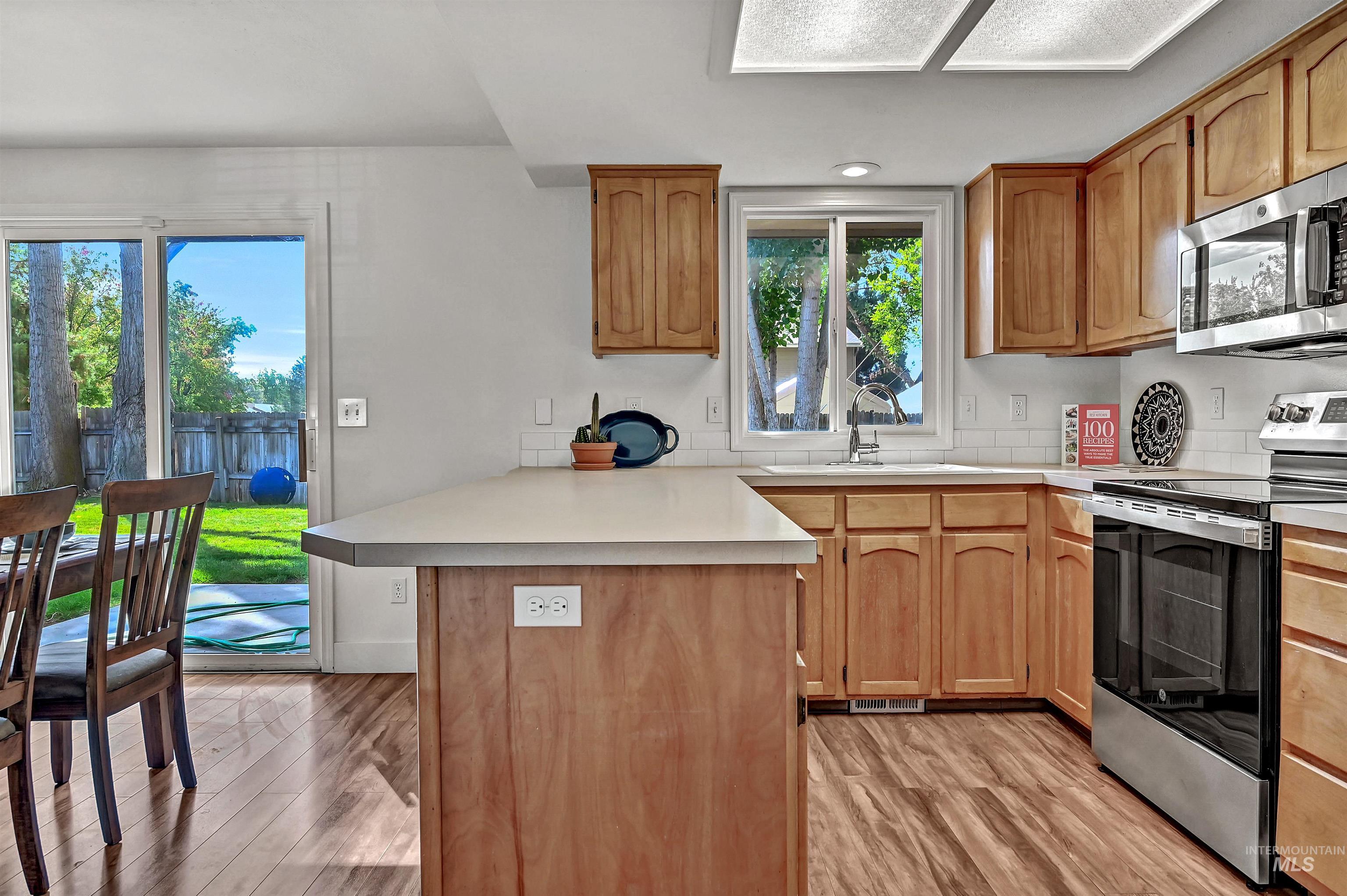 Kitchen with stainless steel appliances, a peninsula, light countertops, and light wood-style floors