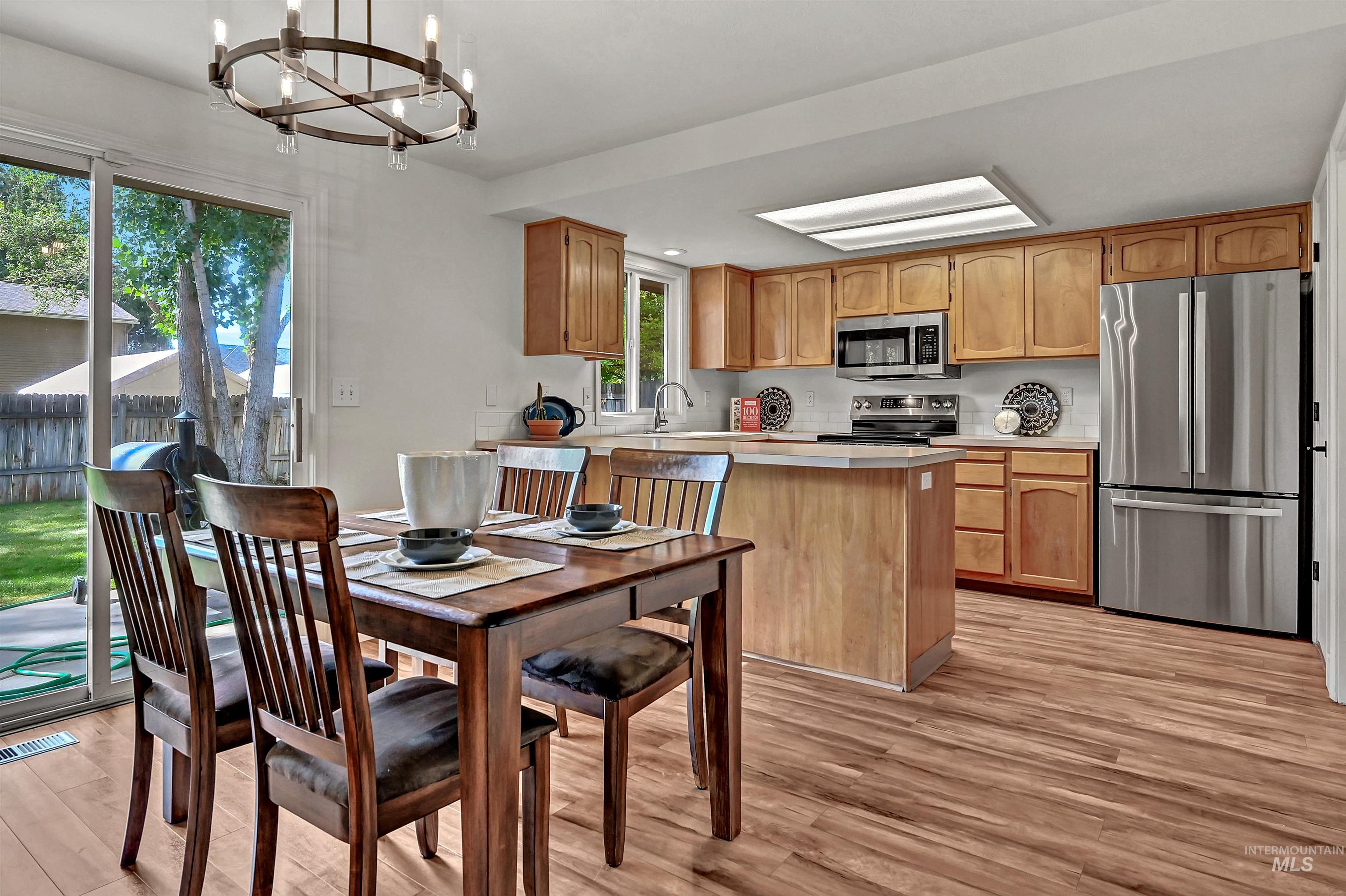 Kitchen & dining area with light countertops, appliances with stainless steel finishes, a peninsula, and light wood-style flooring + a door out to the concrete patio in the backyard