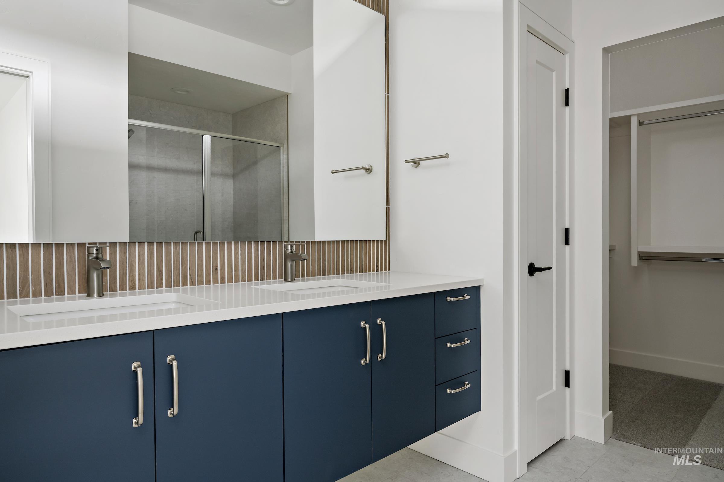 Bathroom with a walk in closet, double vanity, a shower stall, and light tile patterned floors