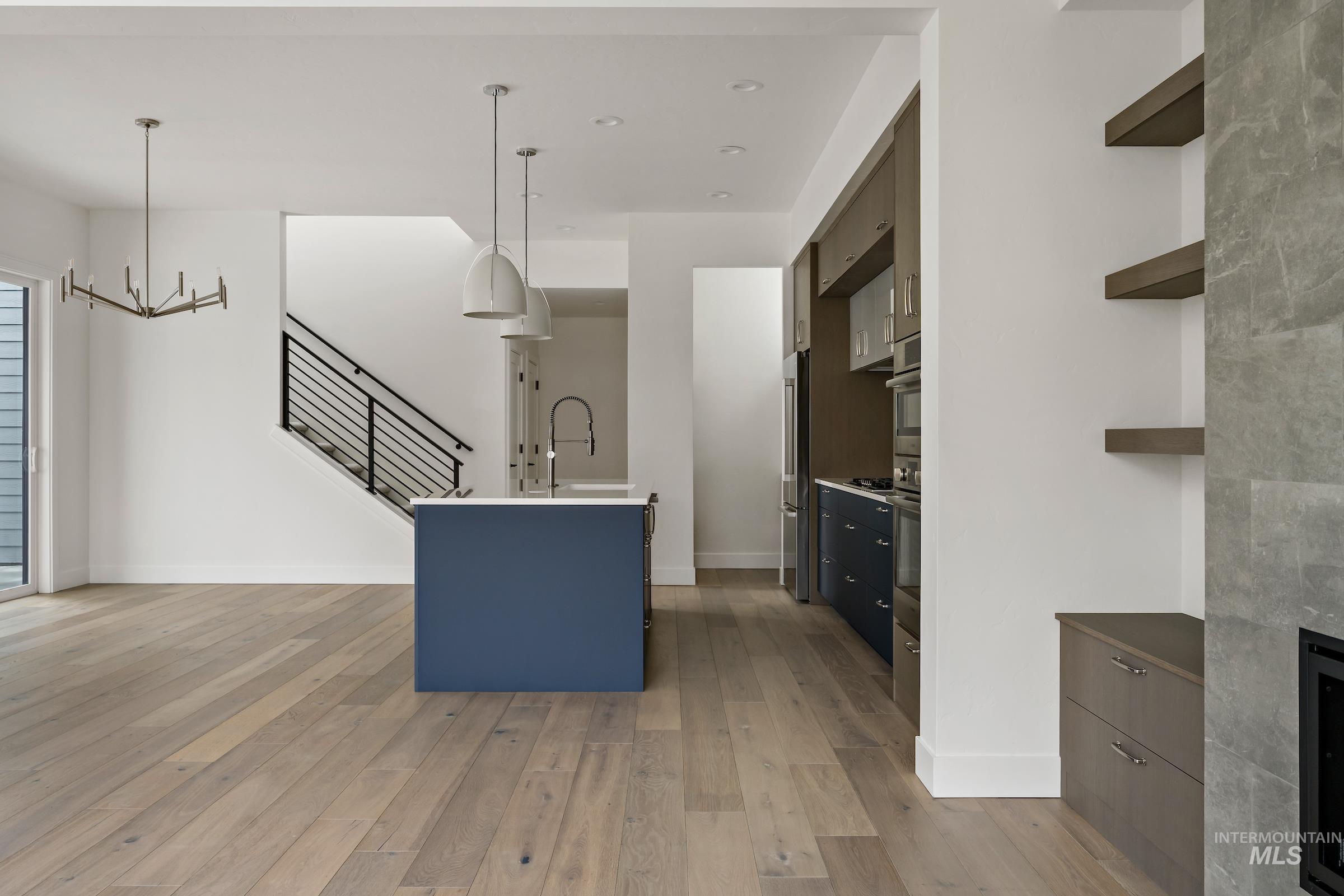 Kitchen featuring decorative light fixtures, light wood-style flooring, a center island with sink, blue cabinetry, and a chandelier