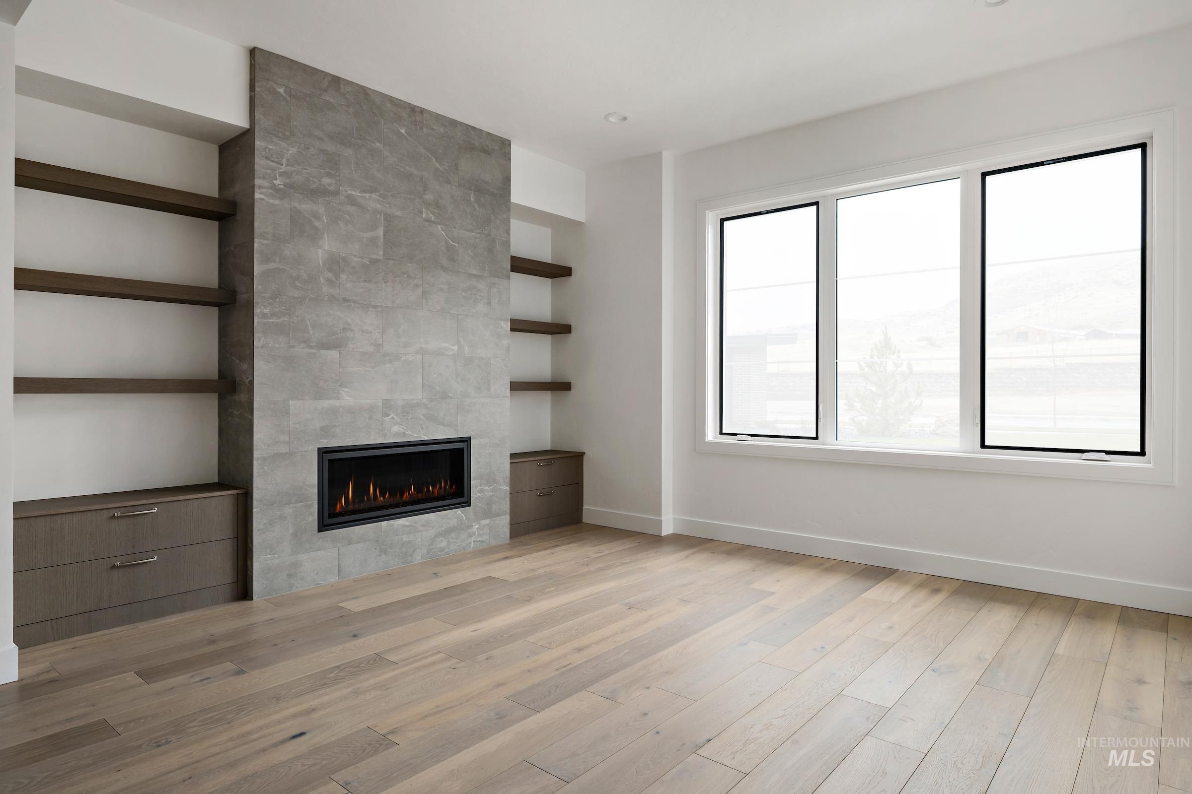 Unfurnished living room featuring built in shelves, a tile fireplace, and light wood-style floors