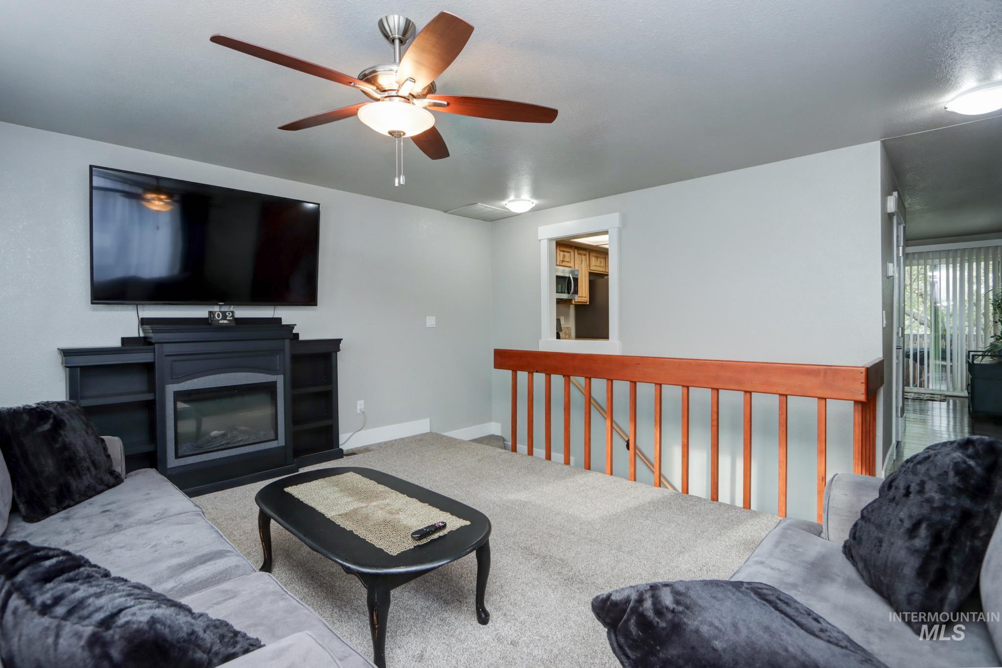 Carpeted living area with ceiling fan and baseboards