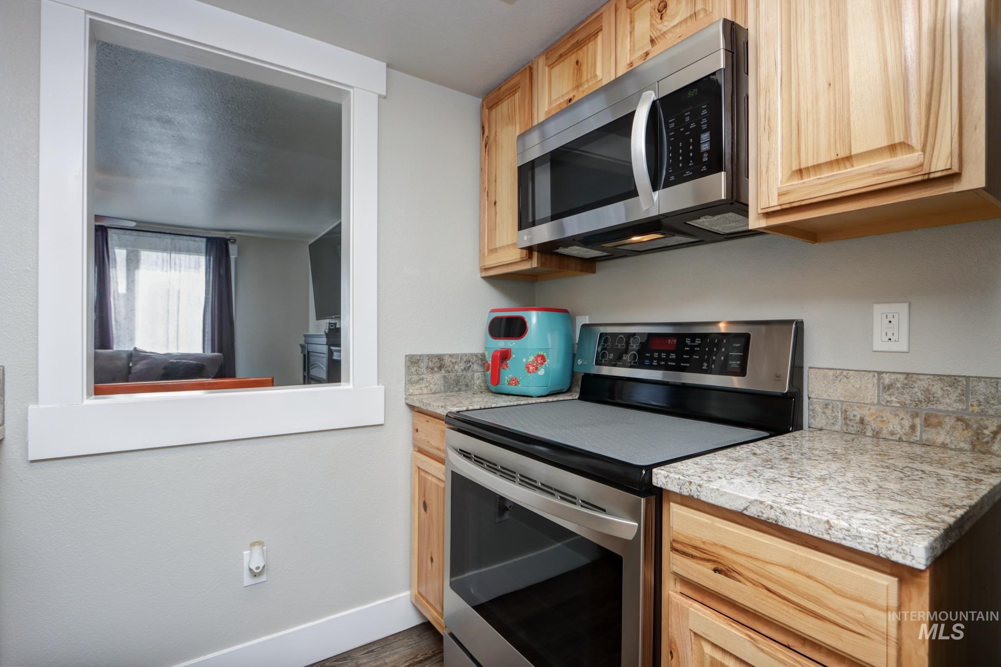Kitchen featuring stainless steel appliances, light wood finish cabinetry, and dark wood-style flooring