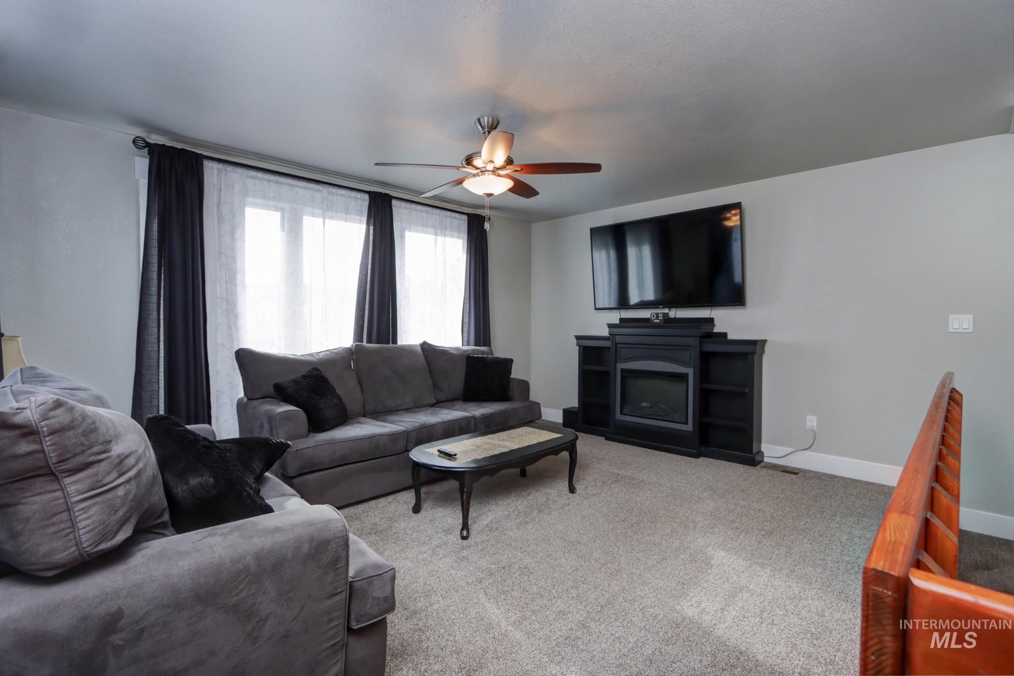Carpeted living area with ceiling fan and baseboards